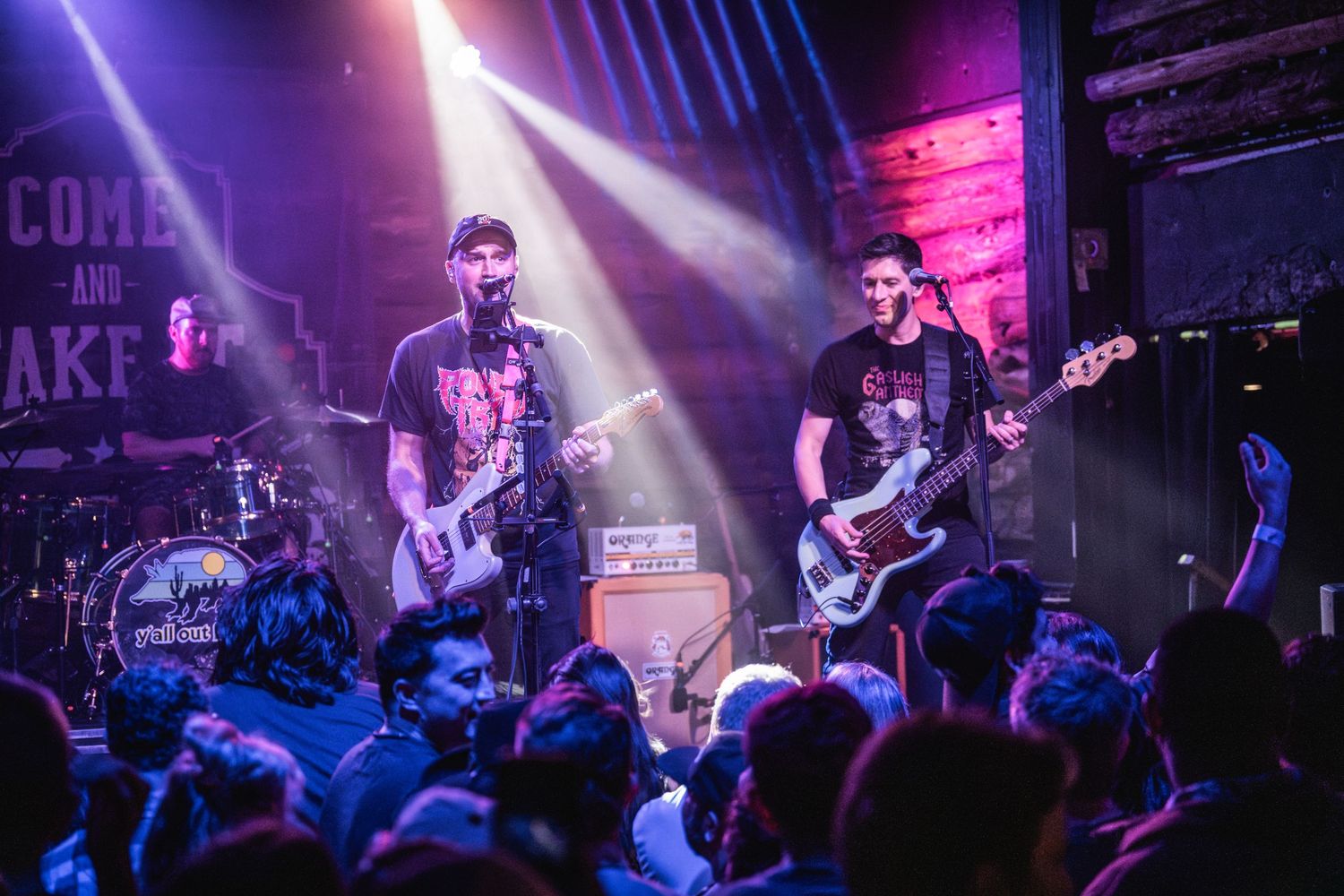 Band members perform on stage with dramatic purple and blue lighting effects.