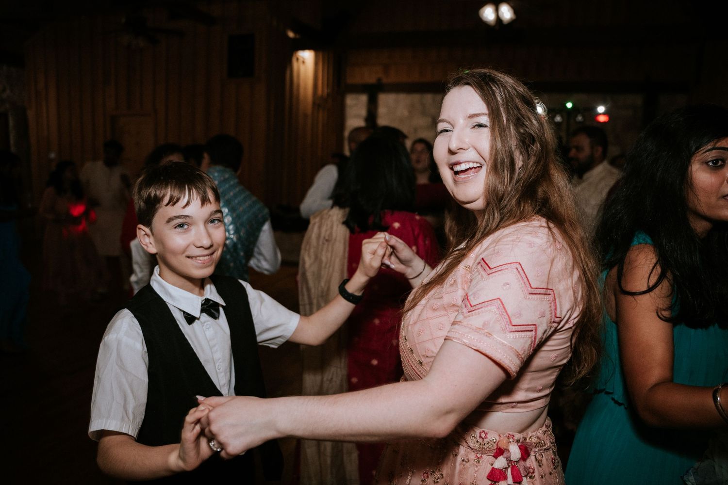 Two guests share a joyful dance moment at a wedding reception in a rustic wooden venue.