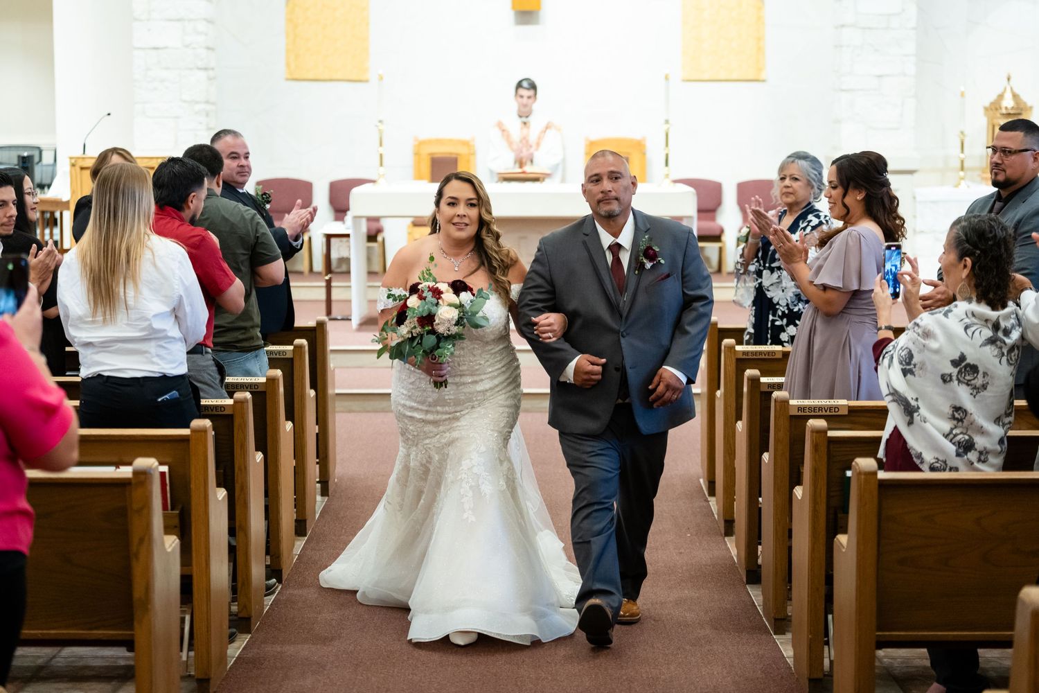 Wedding recessional down church aisle with guests seated in wooden pews.