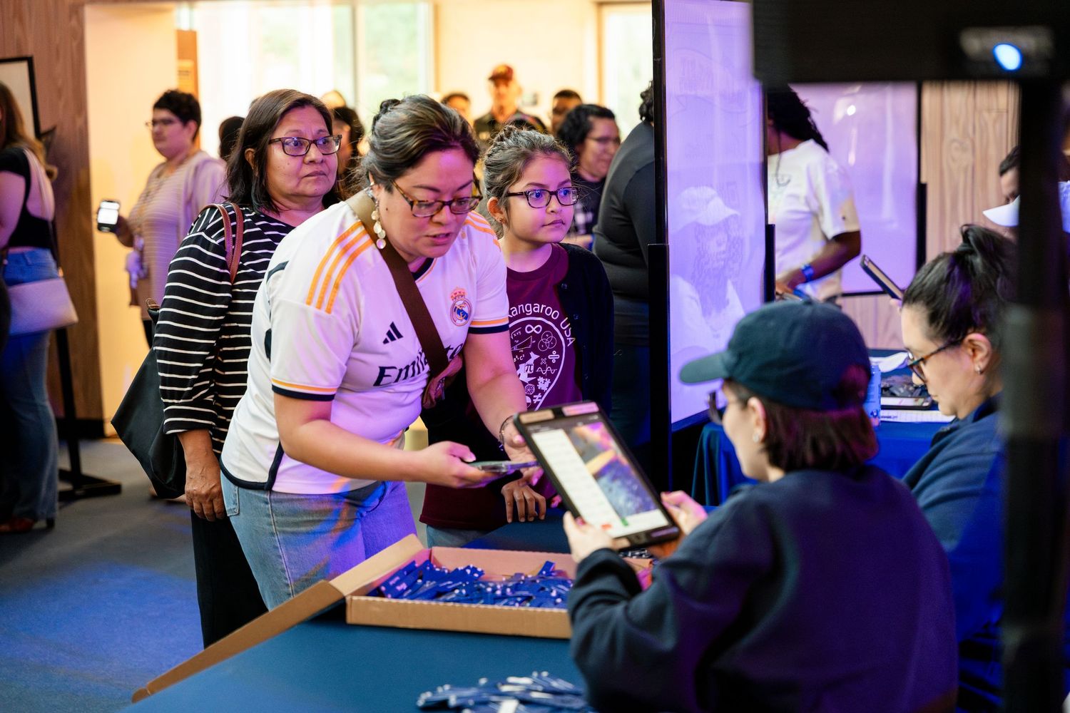 Attendees gather around a table at a gaming event with purple lighting in the background.