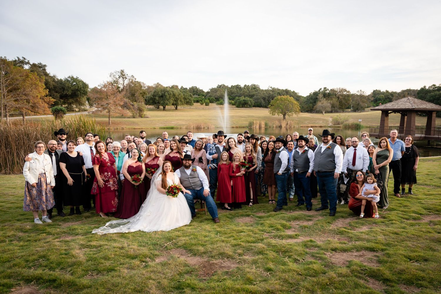 Large wedding party group photo outdoors with burgundy and grey color scheme.