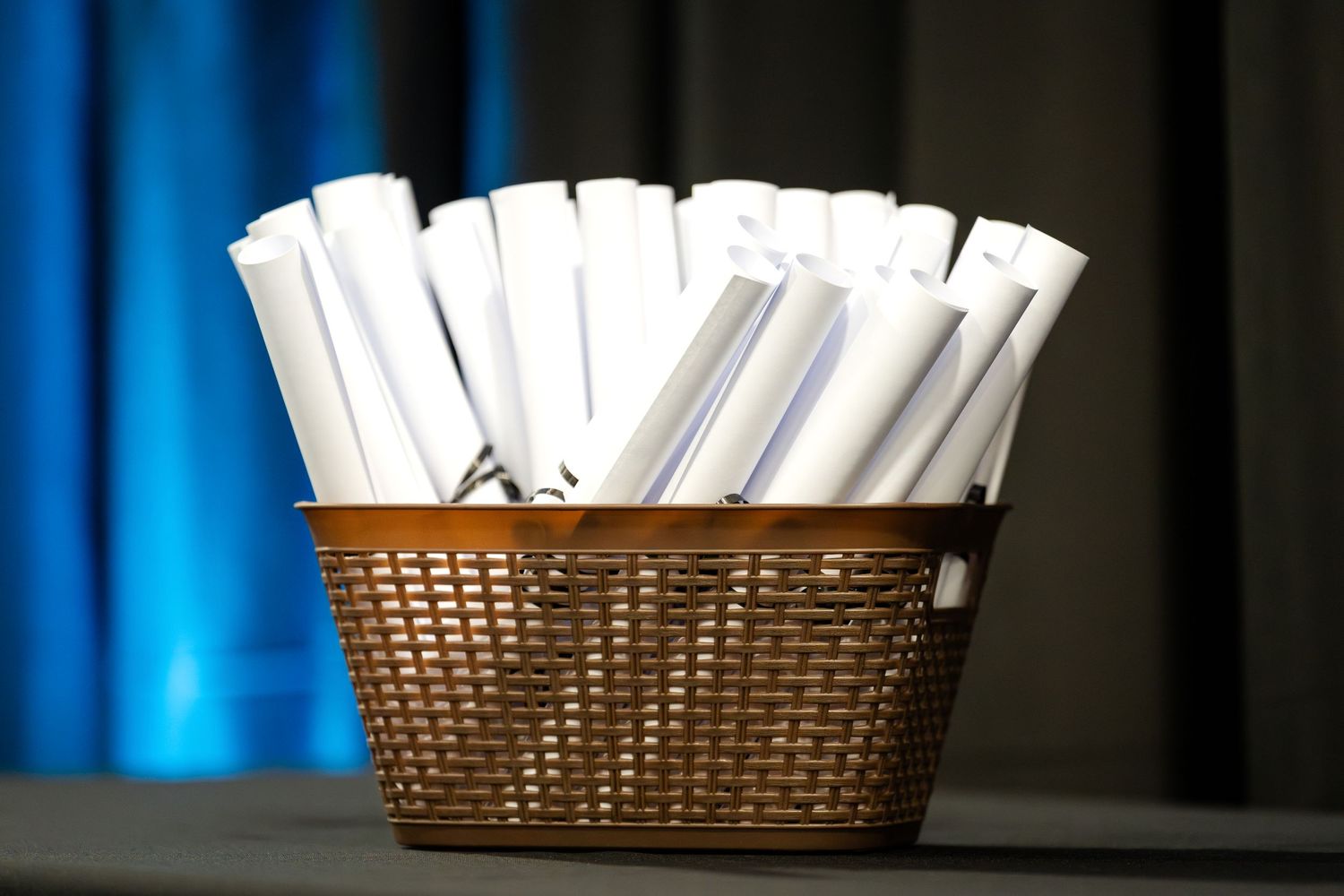 Rolled up diplomas arranged in a woven basket against a blue curtain backdrop.