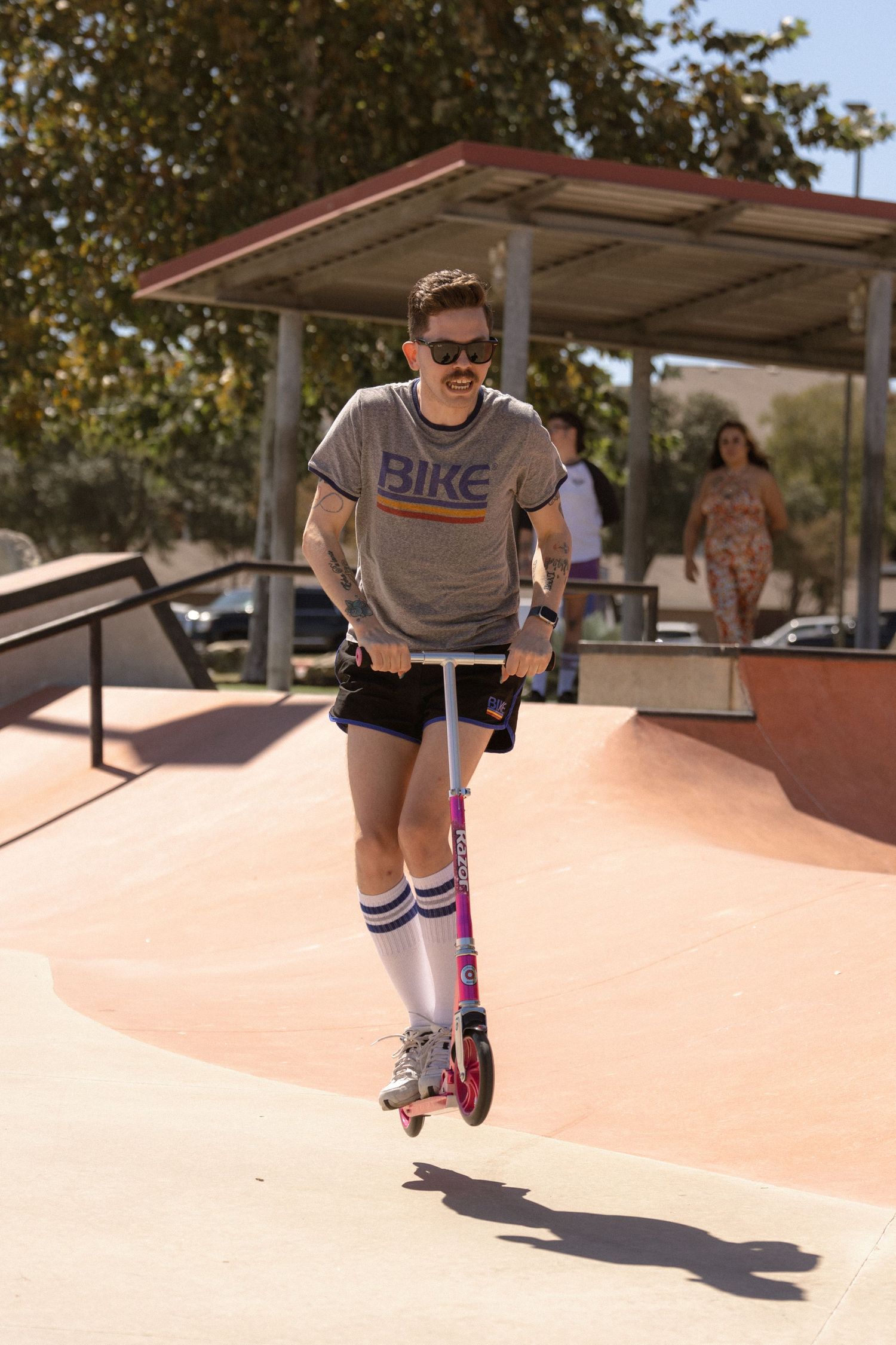 Person riding pink scooter at skate park wearing retro style outfit with tube socks.
