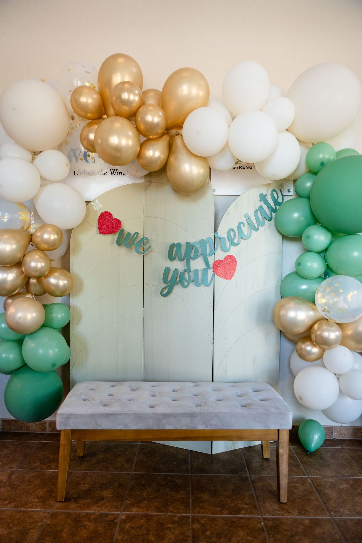 An elegant balloon arch with gold, white and mint green balloons framing an appreciation message.