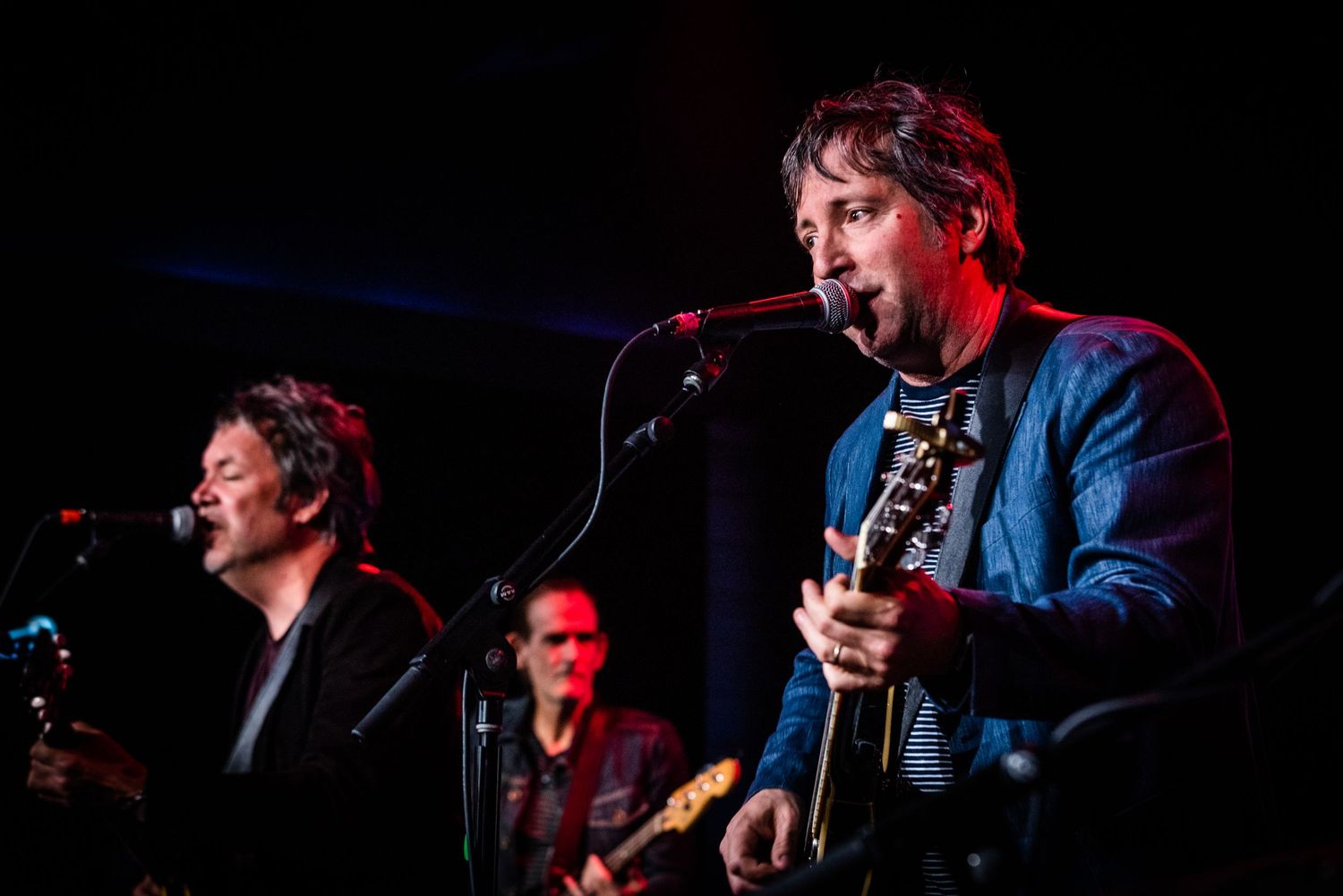 Band members perform together on dimly lit stage with red lighting effects.