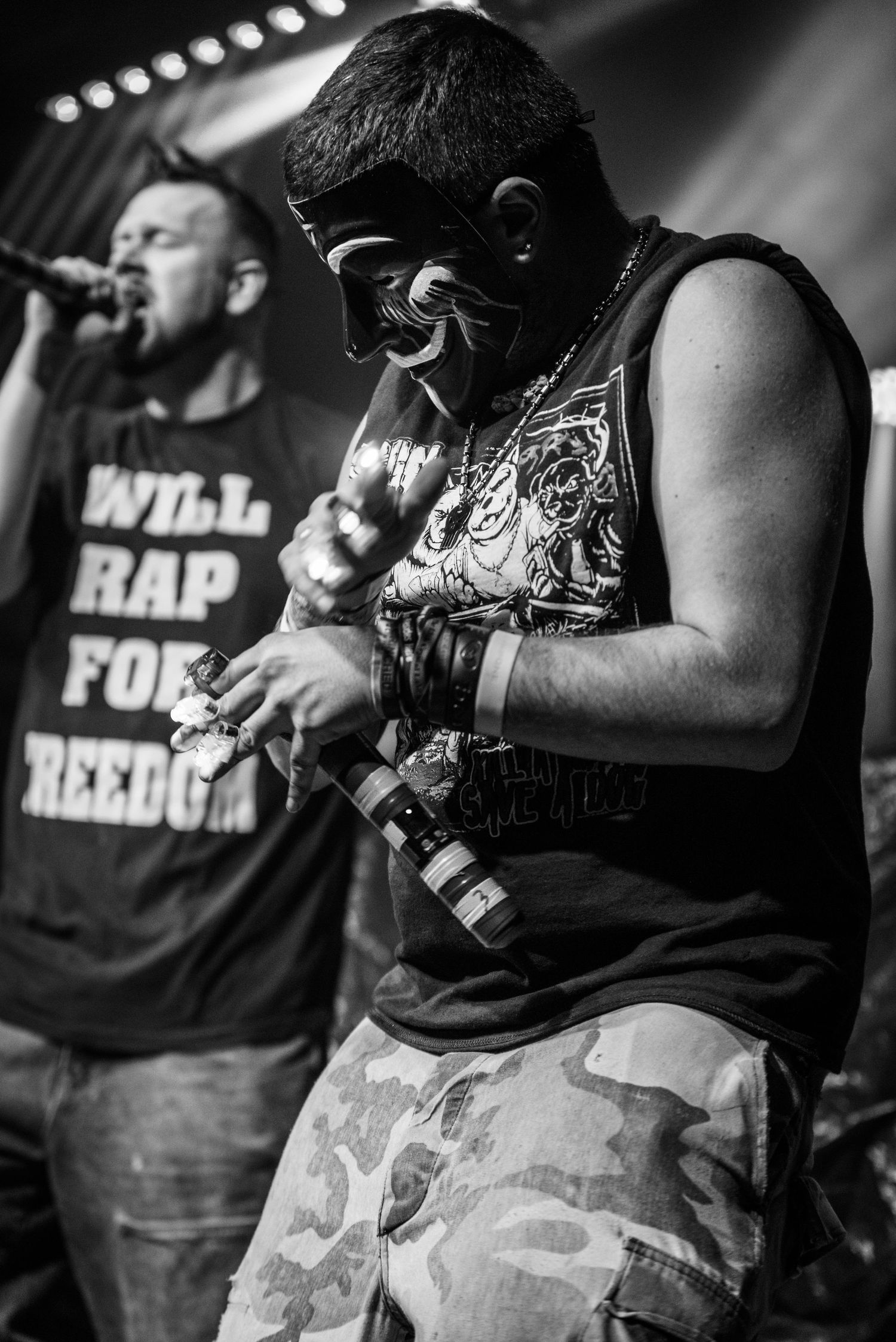 Black and white photo of performers in masks and casual attire during hip hop concert.