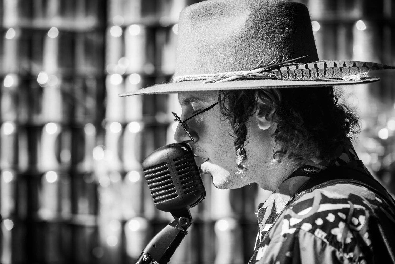 Black and white image of a performer singing into a vintage microphone while wearing a fedora.