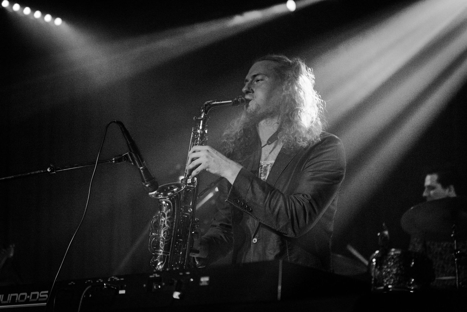 A saxophonist performs on stage under dramatic lighting.