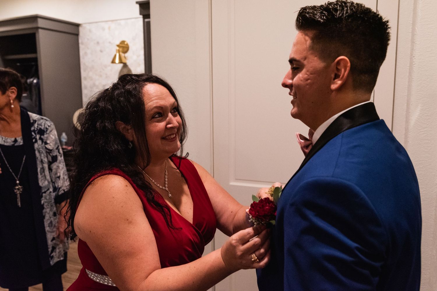 Wedding attendants helping with formal attire preparations indoors.