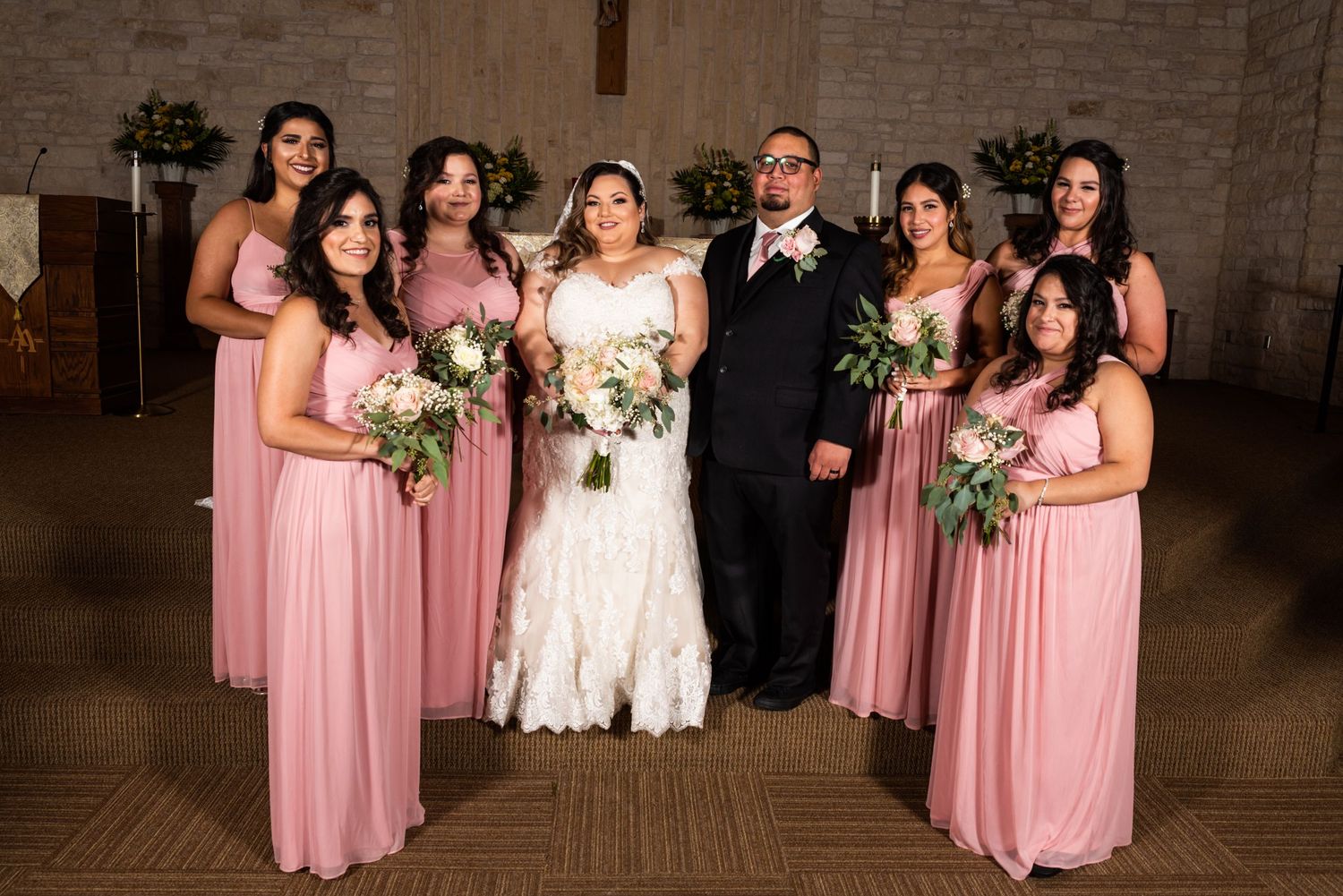 Wedding party poses in church with bridesmaids in pink dresses and couple in center.