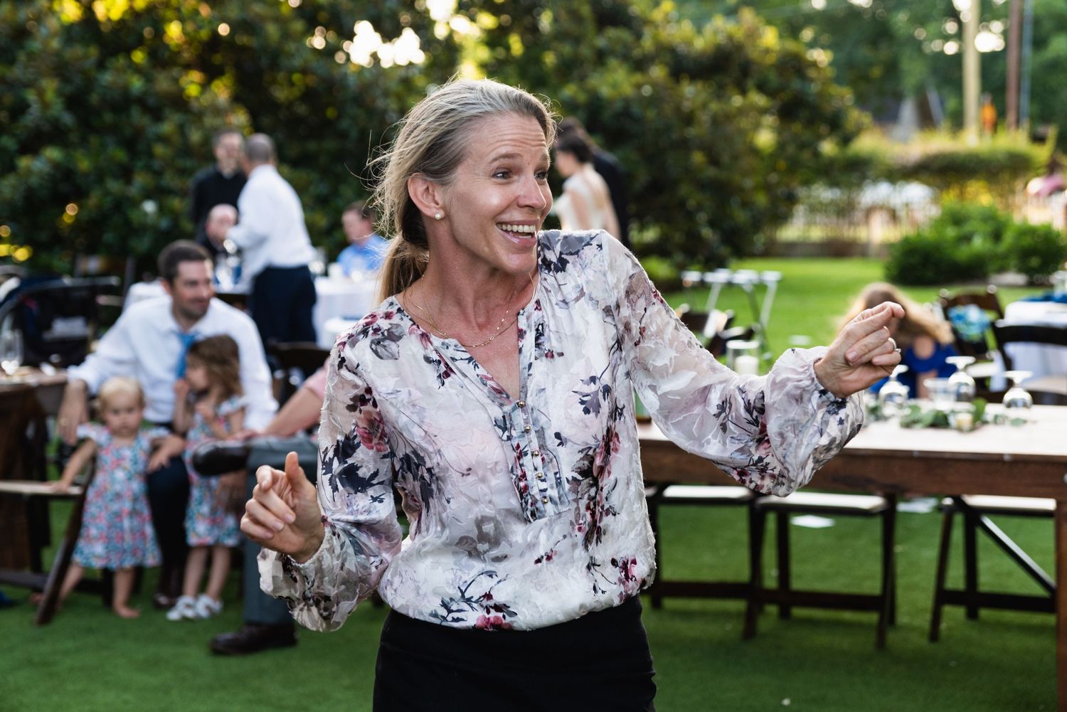 A guest dancing enthusiastically at an outdoor garden reception with tables in background.