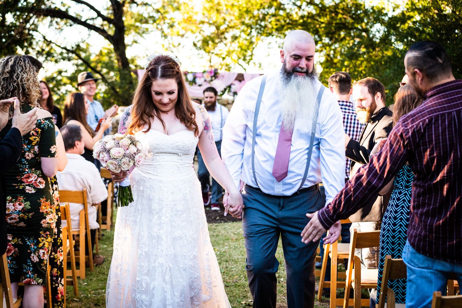Newlyweds walking down aisle at outdoor garden wedding with wooden chairs.