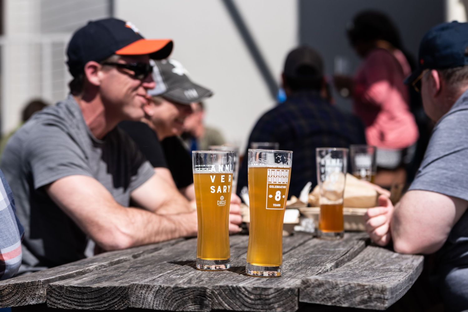 Glasses of golden craft beer on wooden table at outdoor patio.