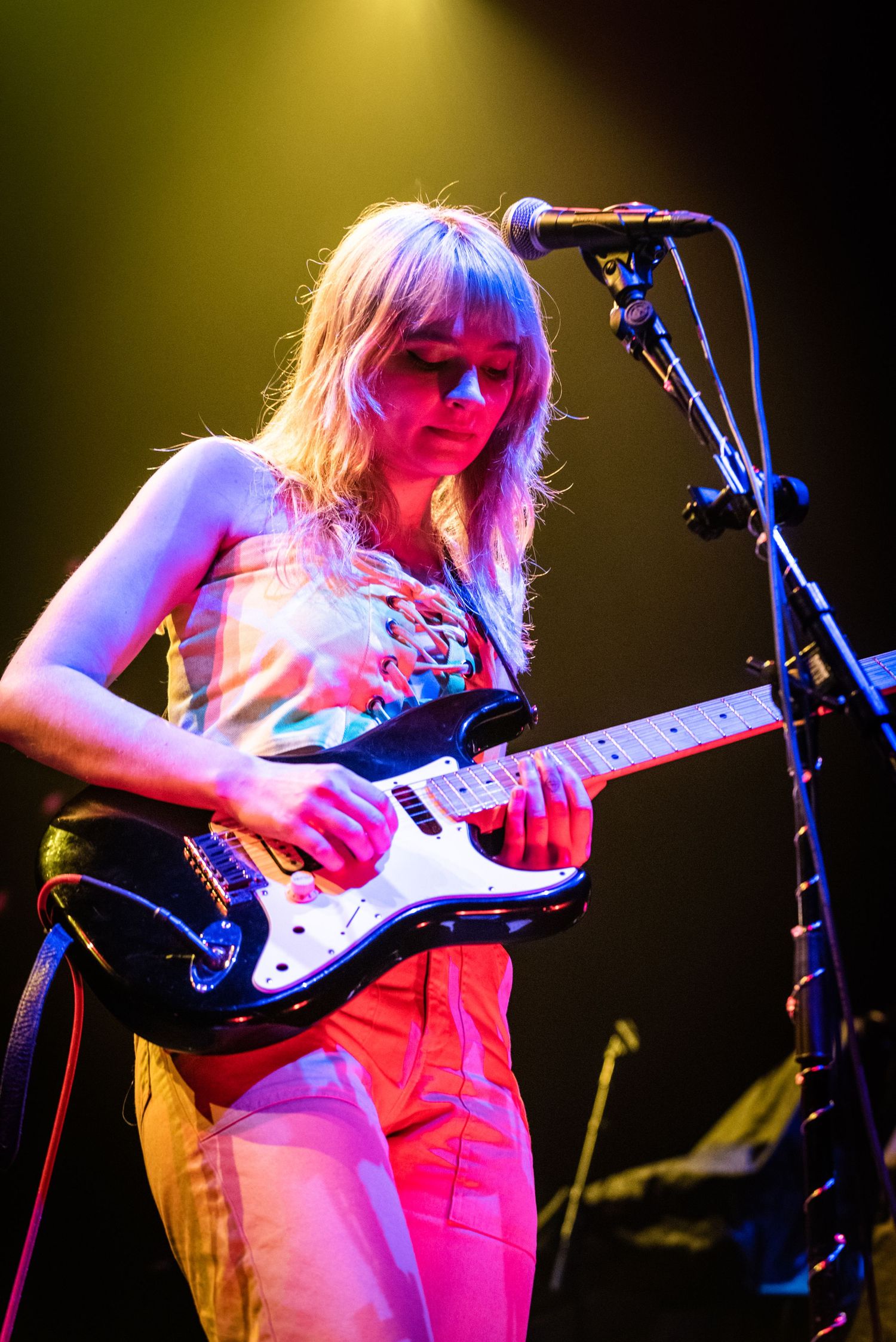 Performer plays electric guitar on stage under vibrant lighting effects.