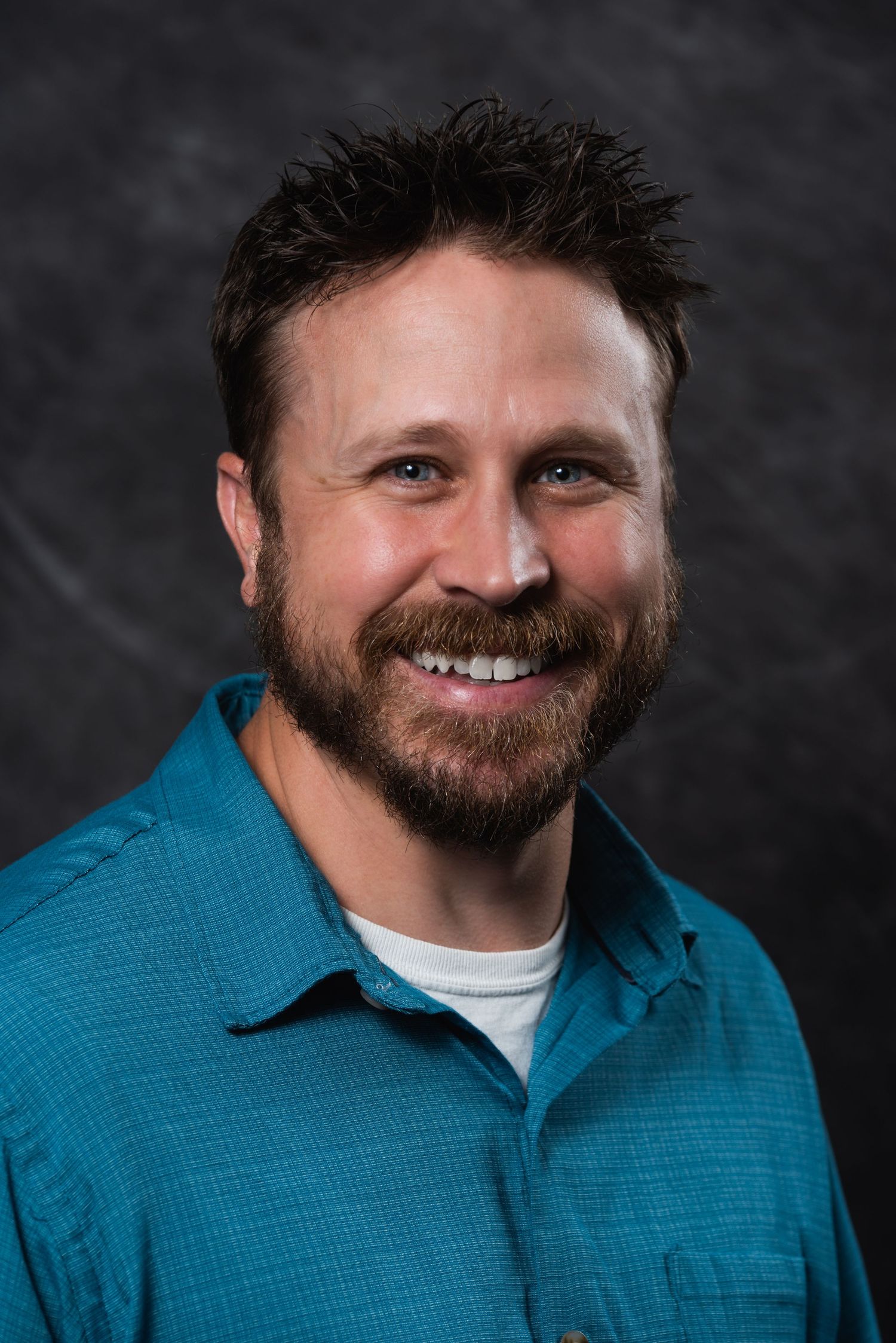 Person in teal collared shirt poses against dark background.