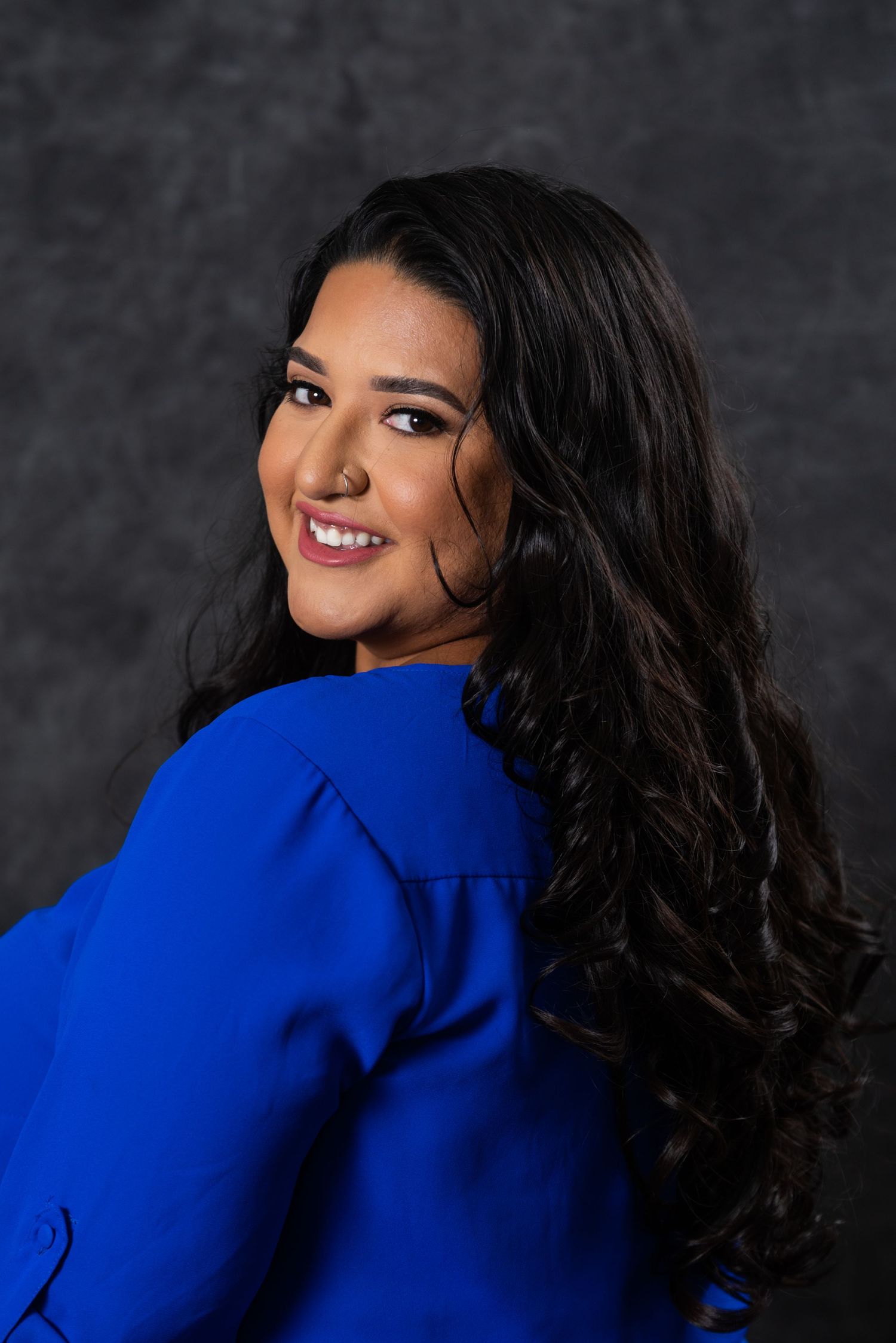 Cheerful pose in royal blue outfit with perfectly styled dark waves against studio backdrop.