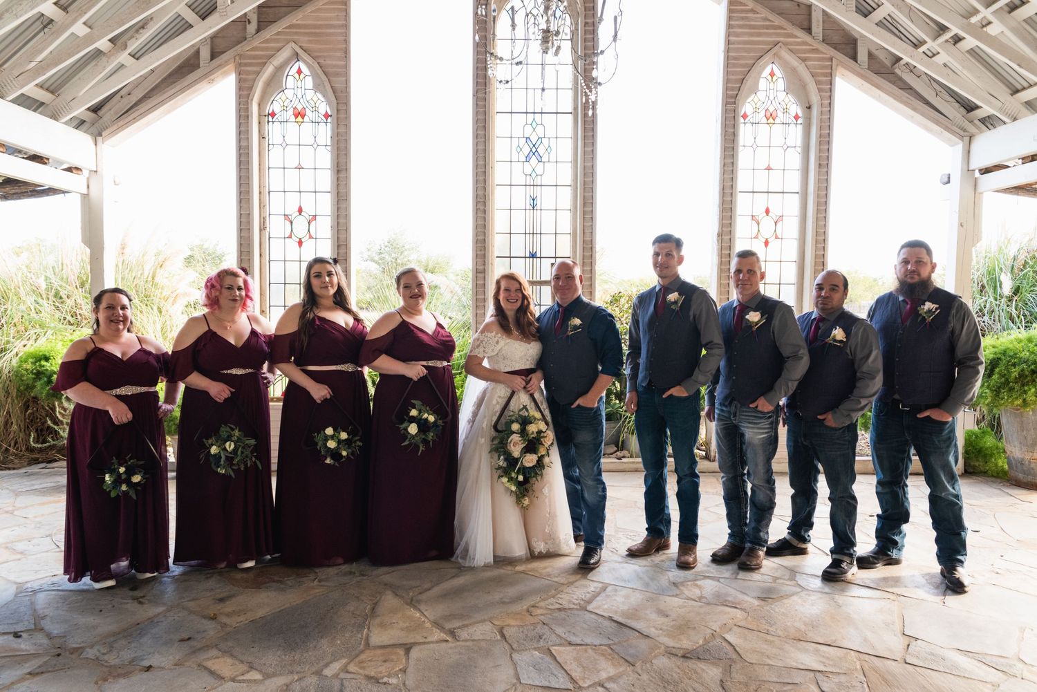 Wedding party in burgundy and navy poses in front of stained glass windows.