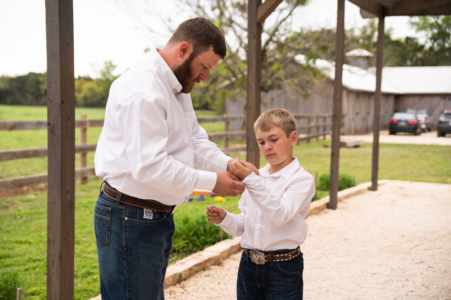 An adult helping a young boy adjust his white dress shirt outdoors.