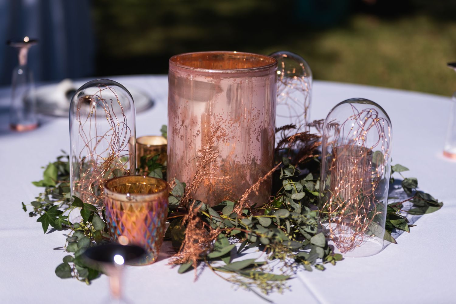 Romantic table centerpiece with glass lanterns and greenery for wedding reception decor.