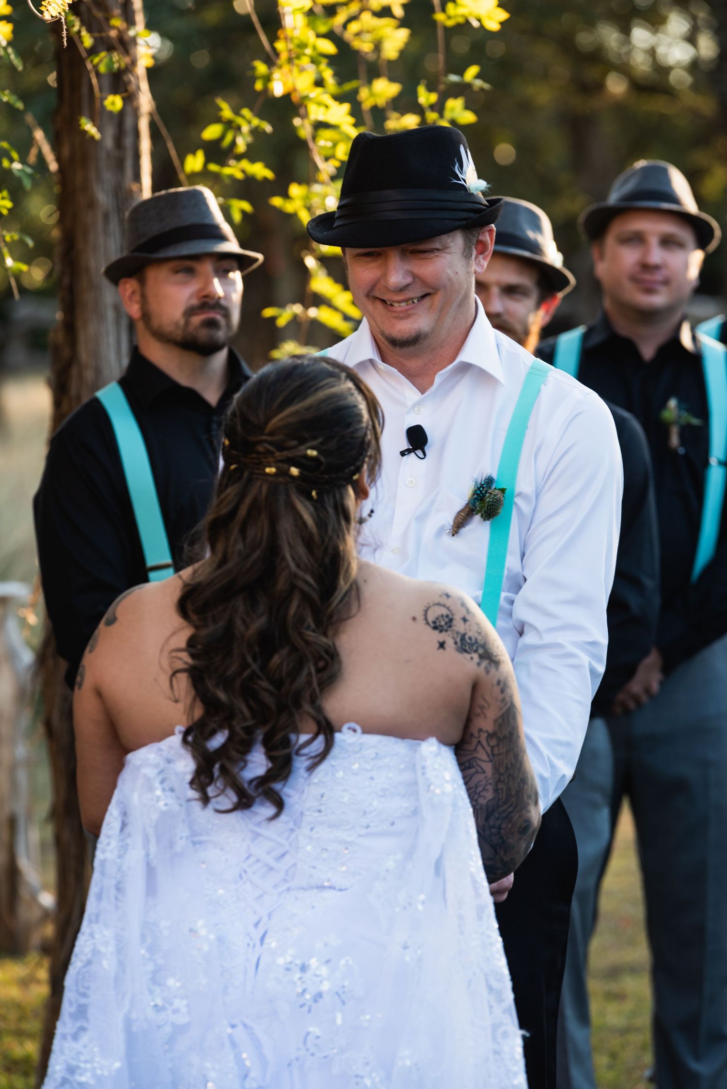 Wedding ceremony moment with groomsmen in black hats and turquoise suspenders.