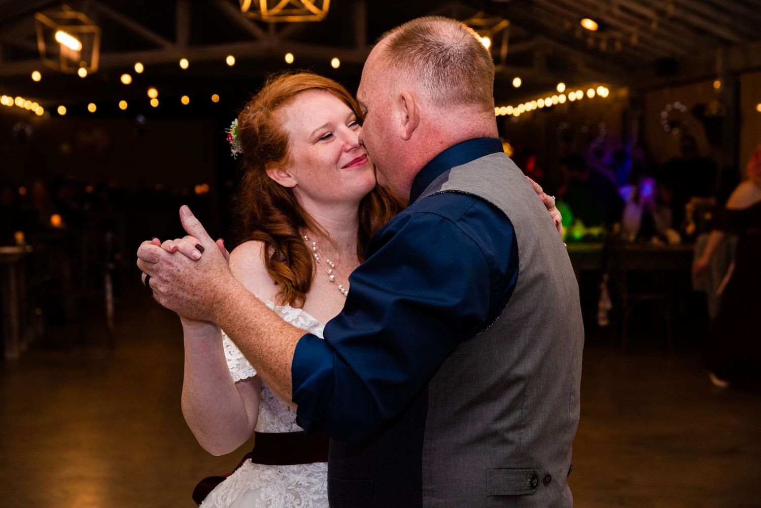 A couple shares a romantic dance moment at their wedding reception under ambient lighting.