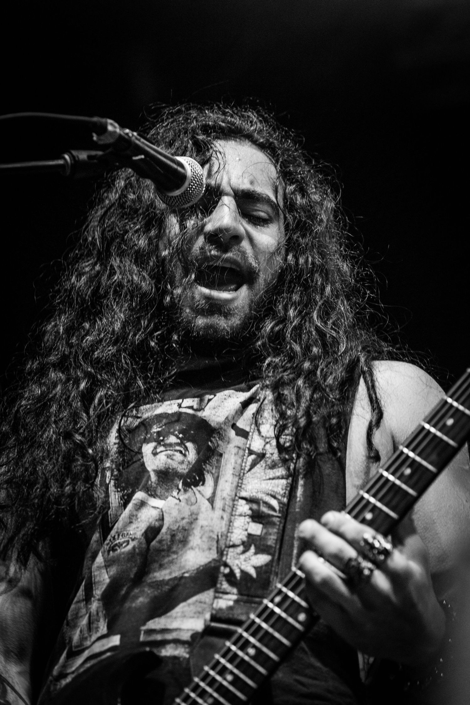 Black and white portrait of guitarist with long hair performing intensely on stage.