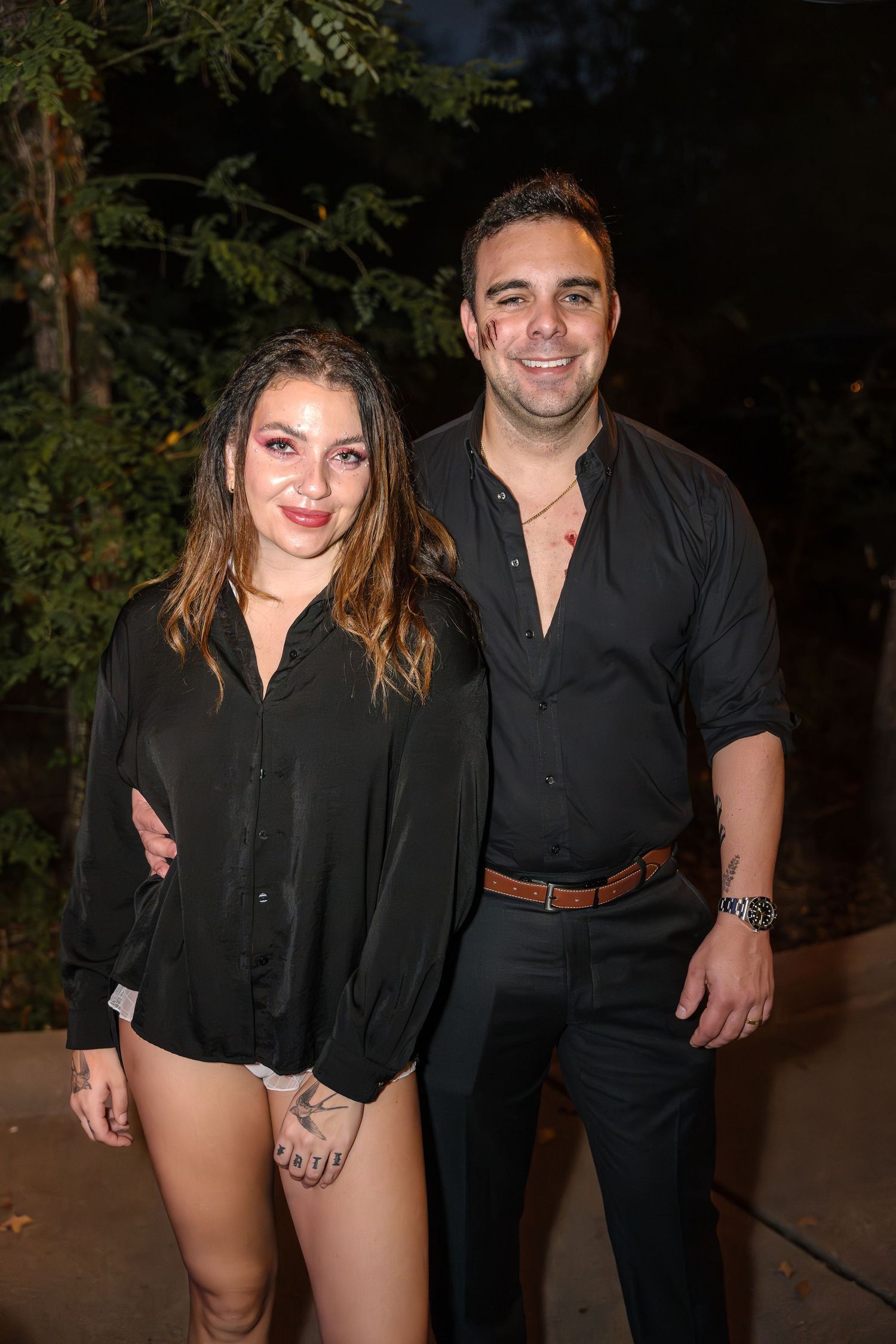 Two people in dark clothing pose together at an evening outdoor event.