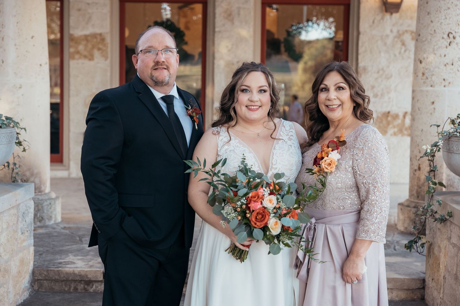 Formal family wedding portrait with fall floral bouquet against stone architecture.