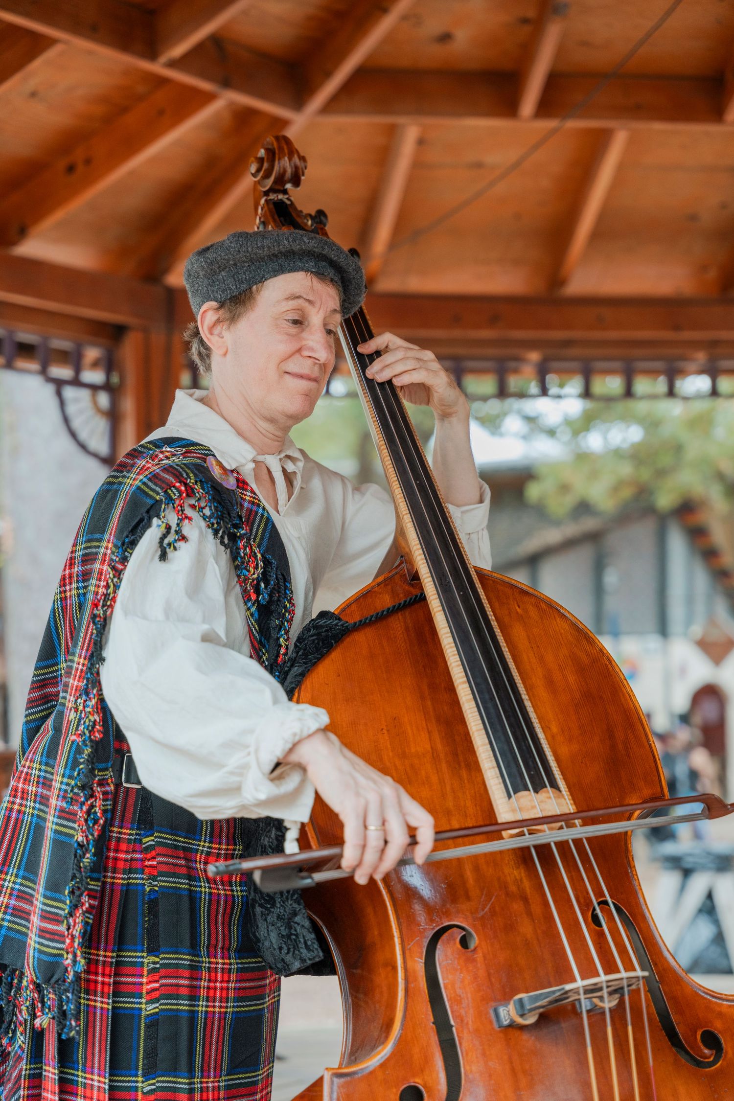 Musician in traditional Scottish attire playing upright bass at renaissance faire.