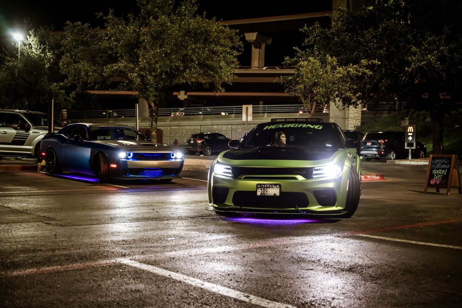 Modified cars with underglow lighting displayed in dark parking lot.