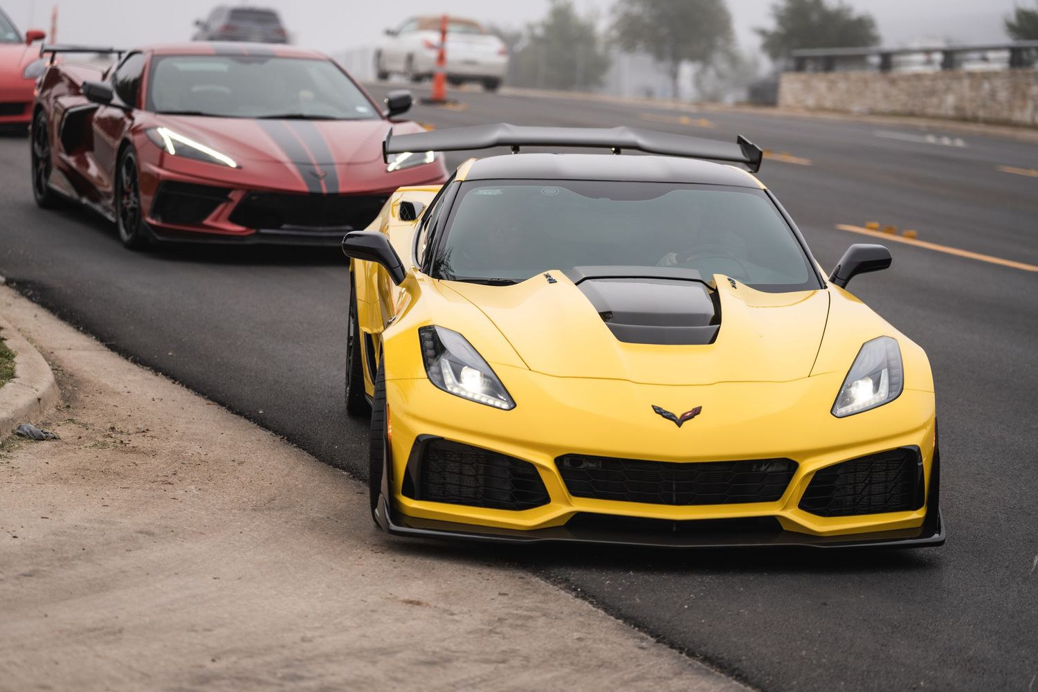 A yellow Chevrolet Corvette ZR1 leads a red sports car on a foggy road.