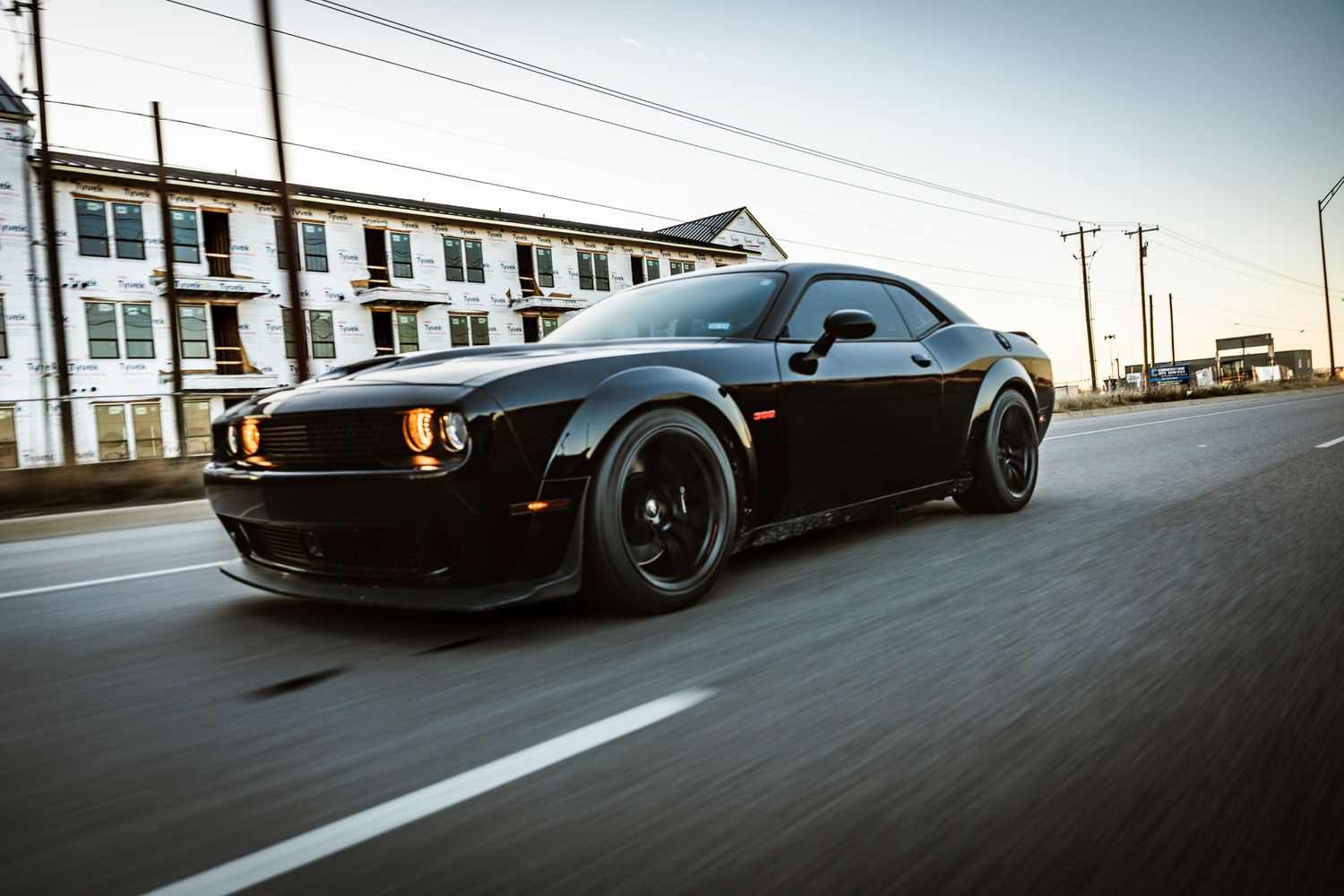 Black Dodge Challenger Hellcat with blacked-out wheels cruising on city street.