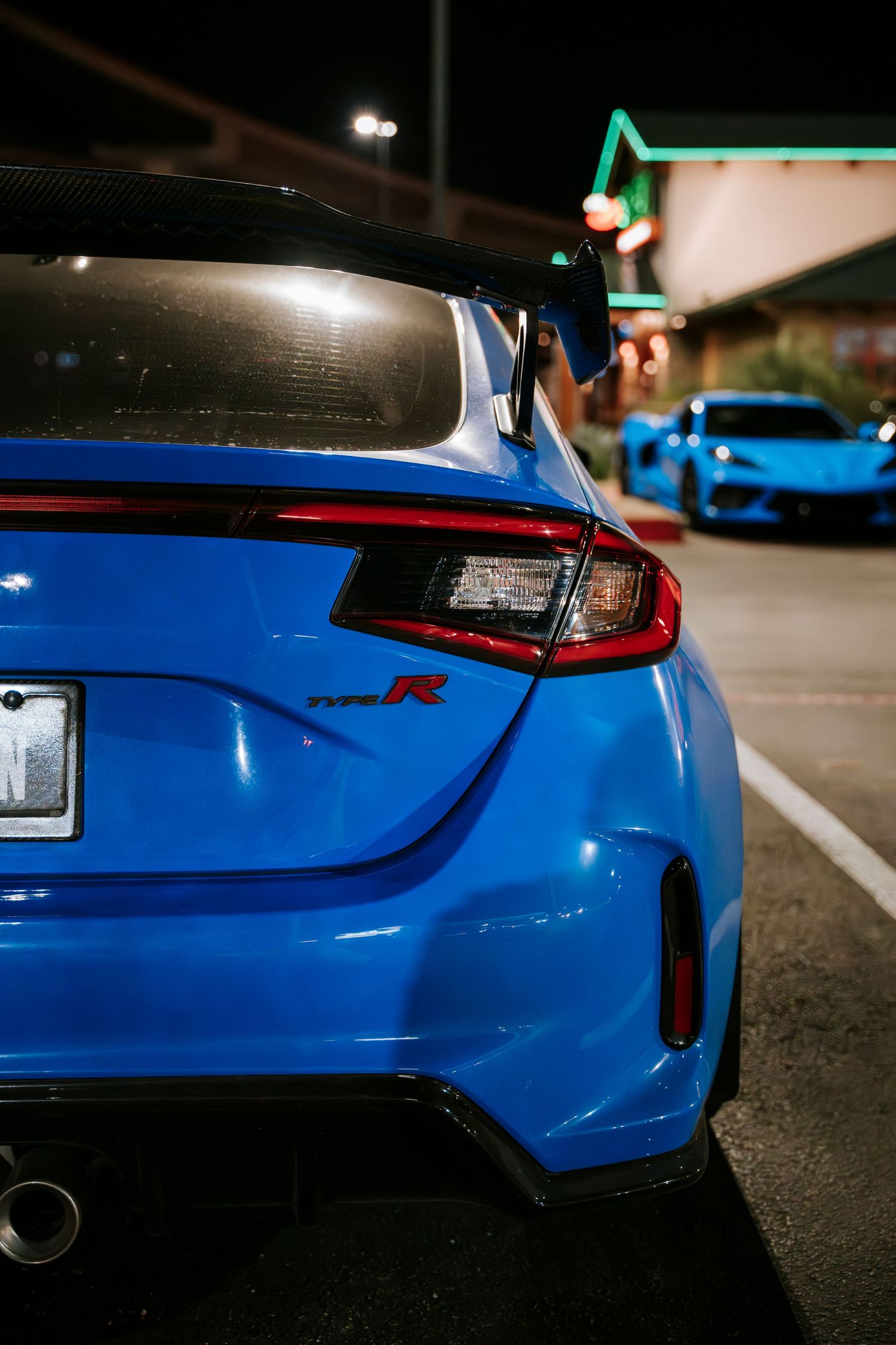 Rear view of a bright blue sports car with modern LED taillights in a parking lot at night.