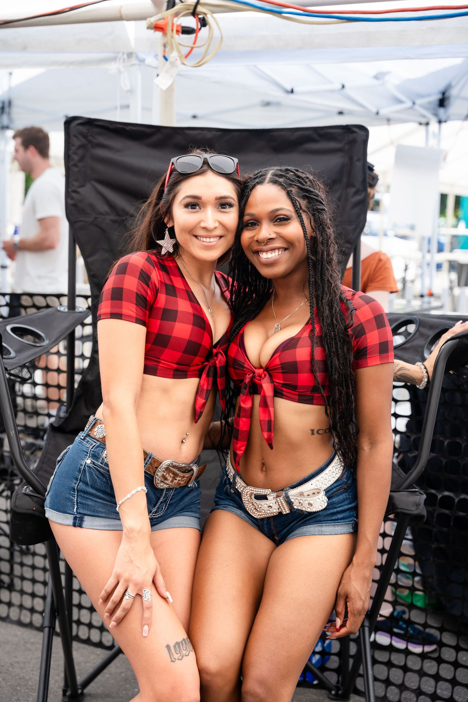 Two friends in matching red plaid crop tops and denim shorts pose at a festival.