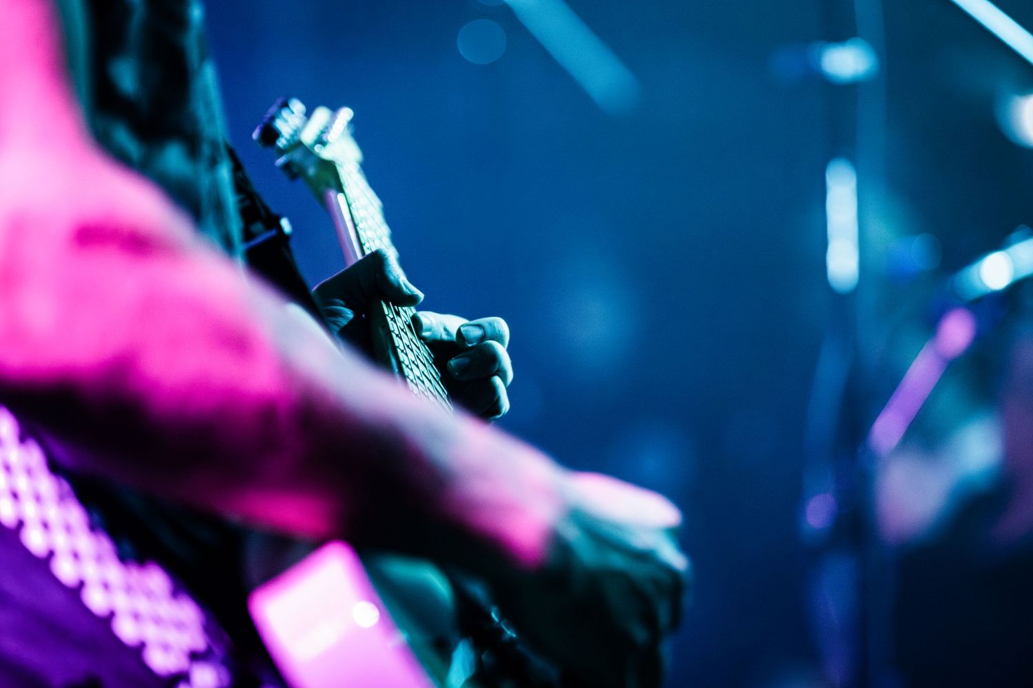 Close-up of guitarist's hands playing electric guitar on stage with colorful lighting.