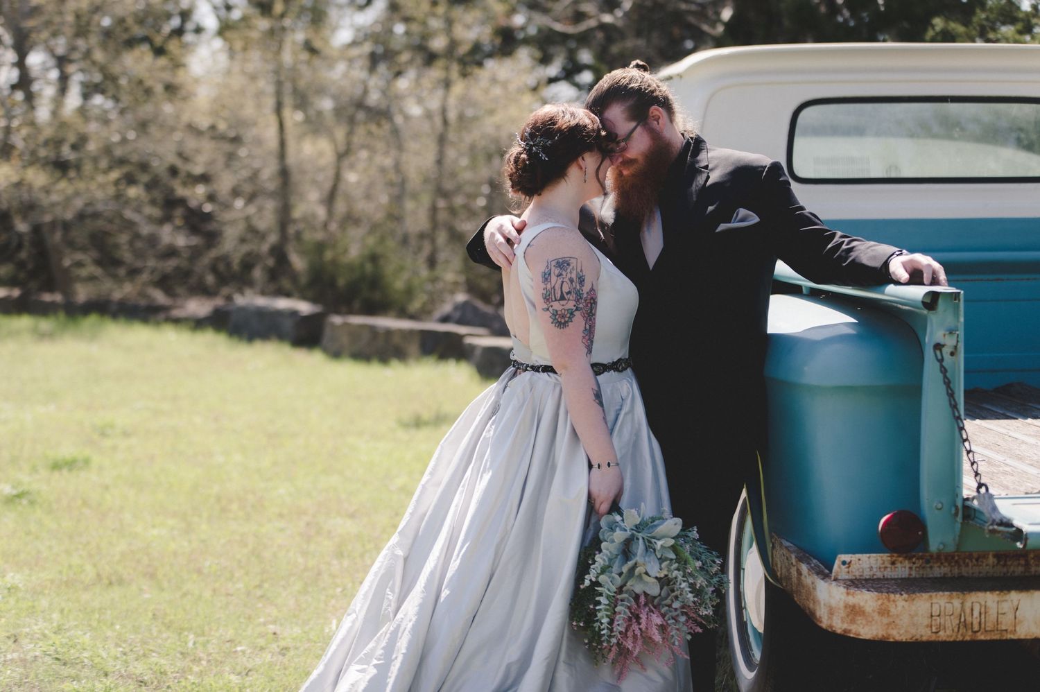 A tender wedding moment captured against a turquoise vintage truck in soft sunlight.