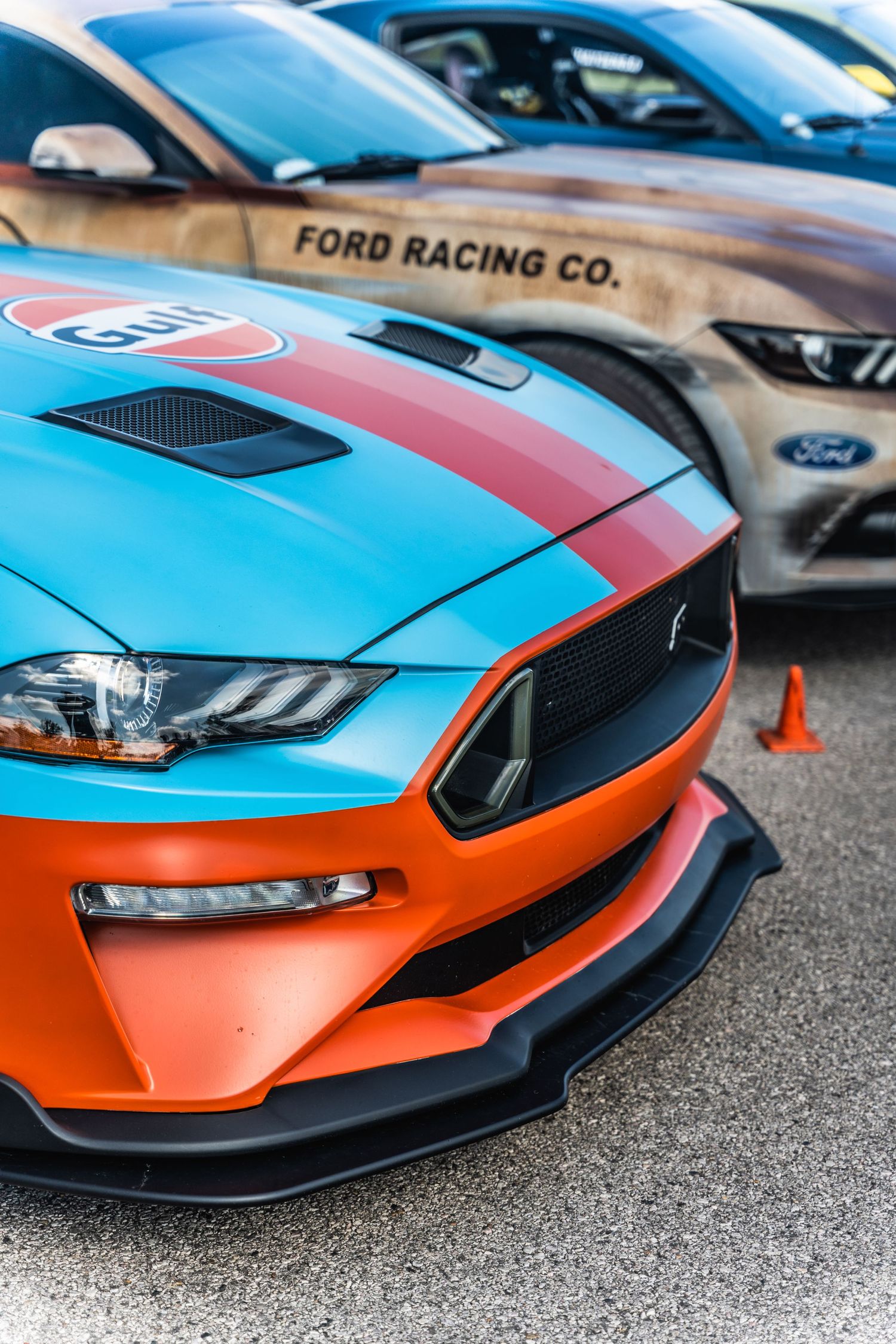 Close-up of a Ford Mustang front end with orange and blue racing stripes and custom body modifications.
