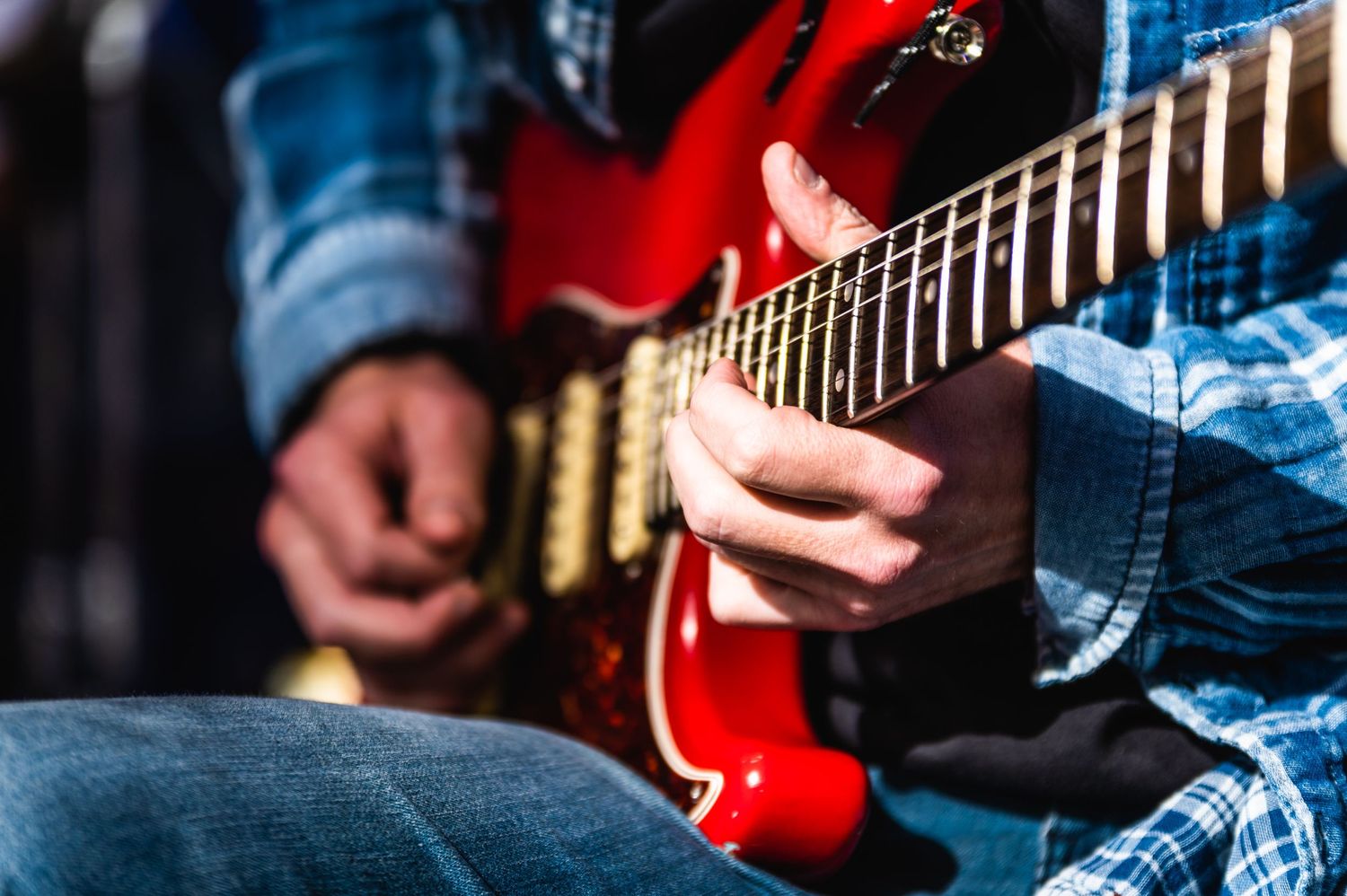 Close-up detail of hands playing red electric guitar strings during performance.