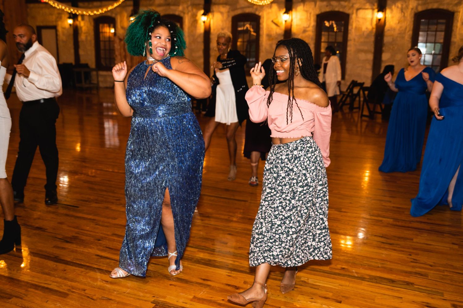 Wedding guests dance enthusiastically on a polished wooden floor under warm venue lighting.