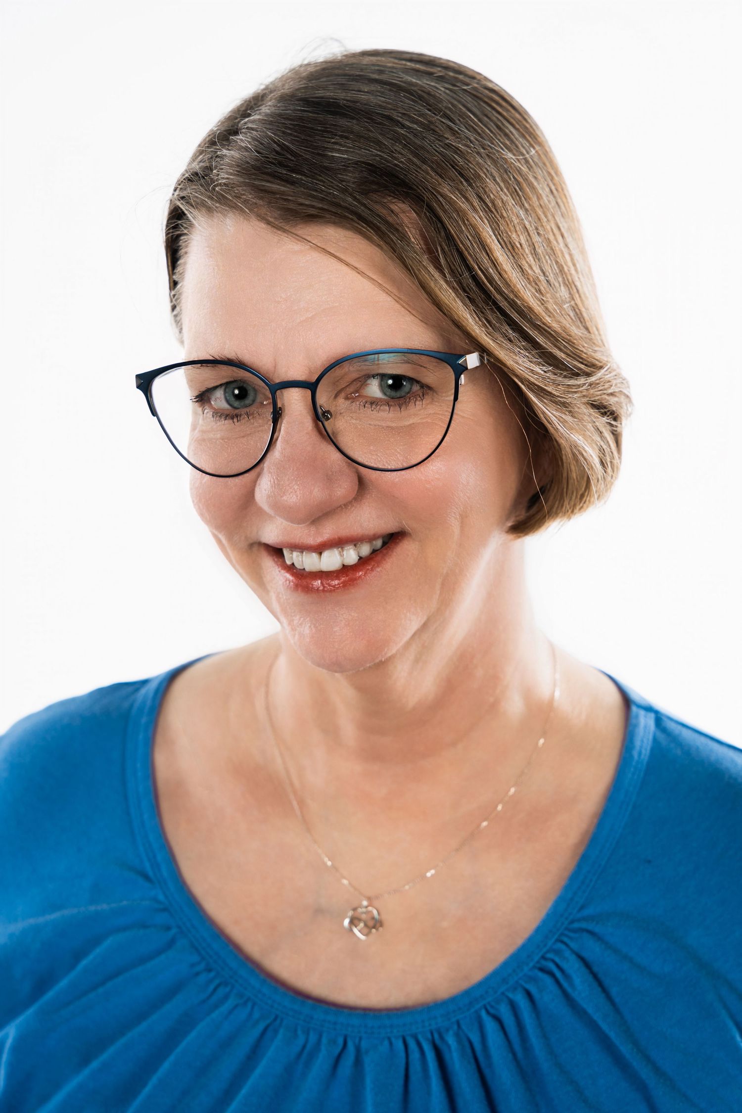 Portrait of person in blue top wearing cat-eye glasses against white background.