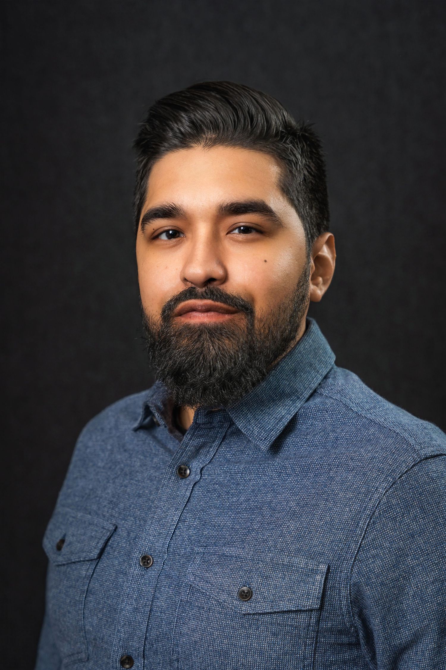 Studio portrait of person in blue denim shirt against dark background.