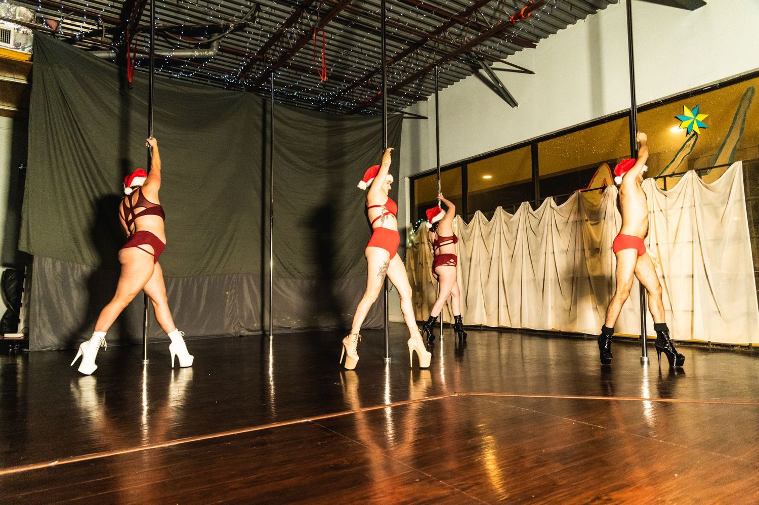 Group of pole dancers performing synchronized routine on stage with festive decorations.