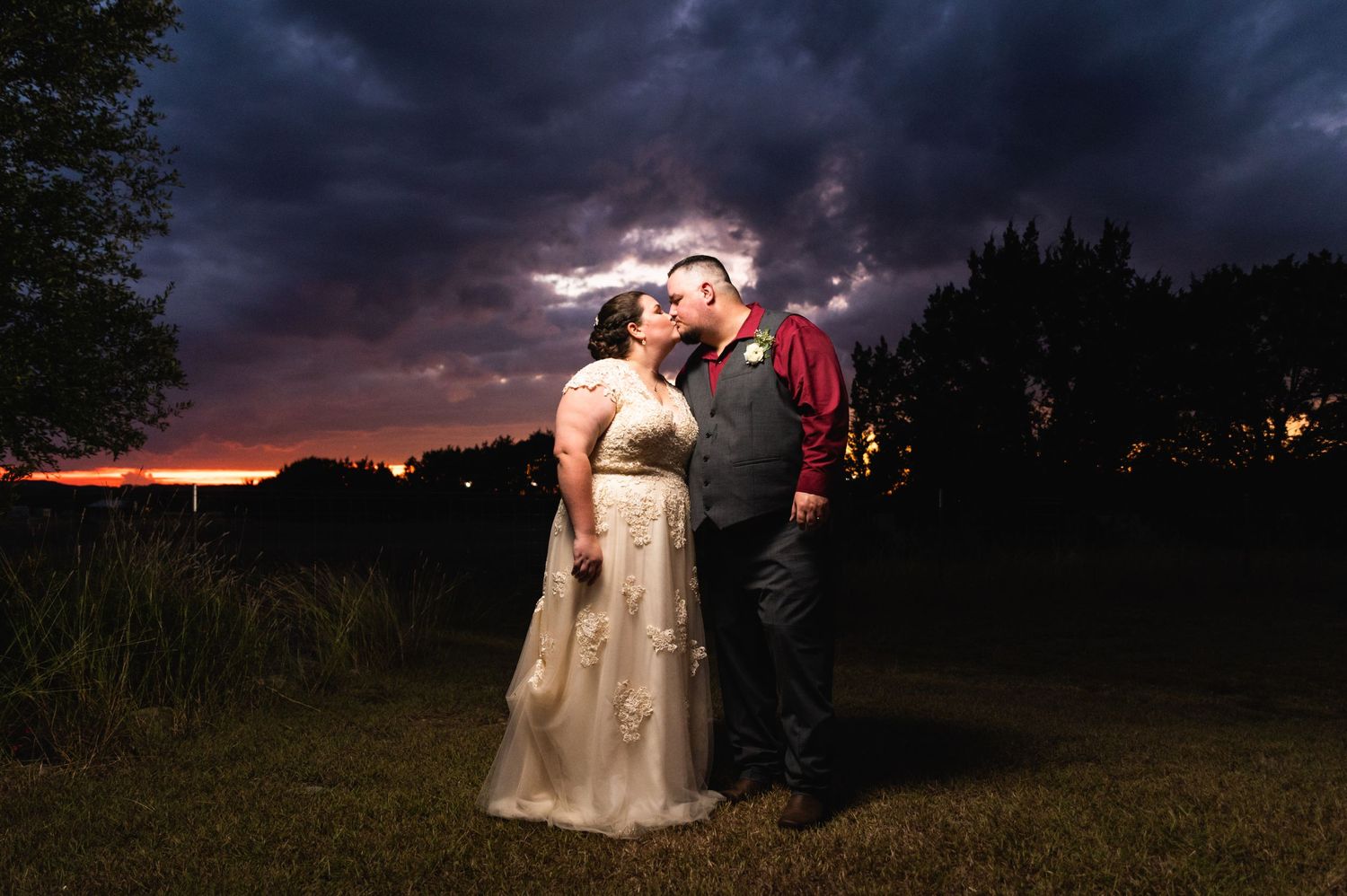 A romantic twilight portrait in front of a dramatic purple stormy sky with silhouetted trees.