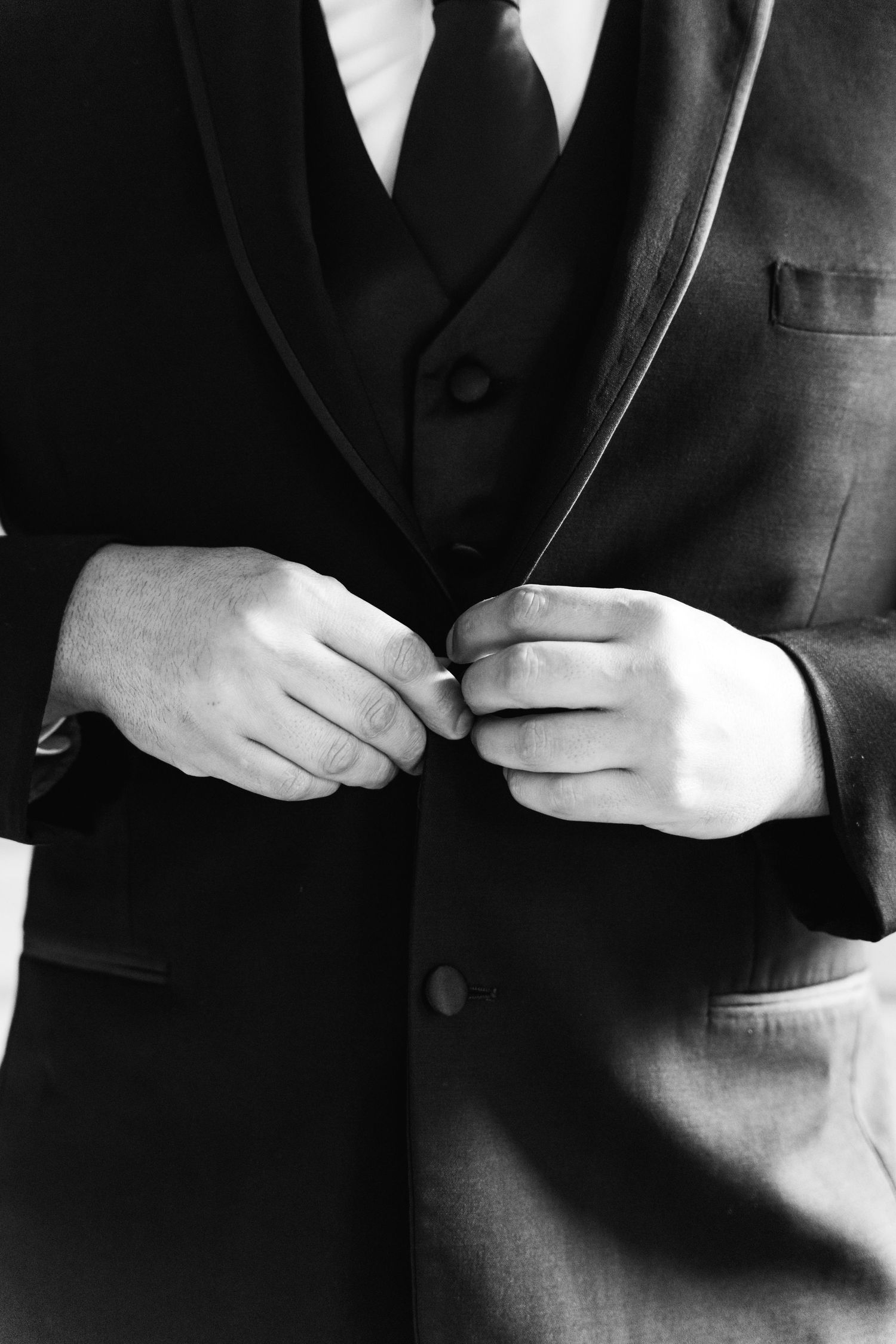 Close up black and white shot of hands buttoning a formal black suit jacket.