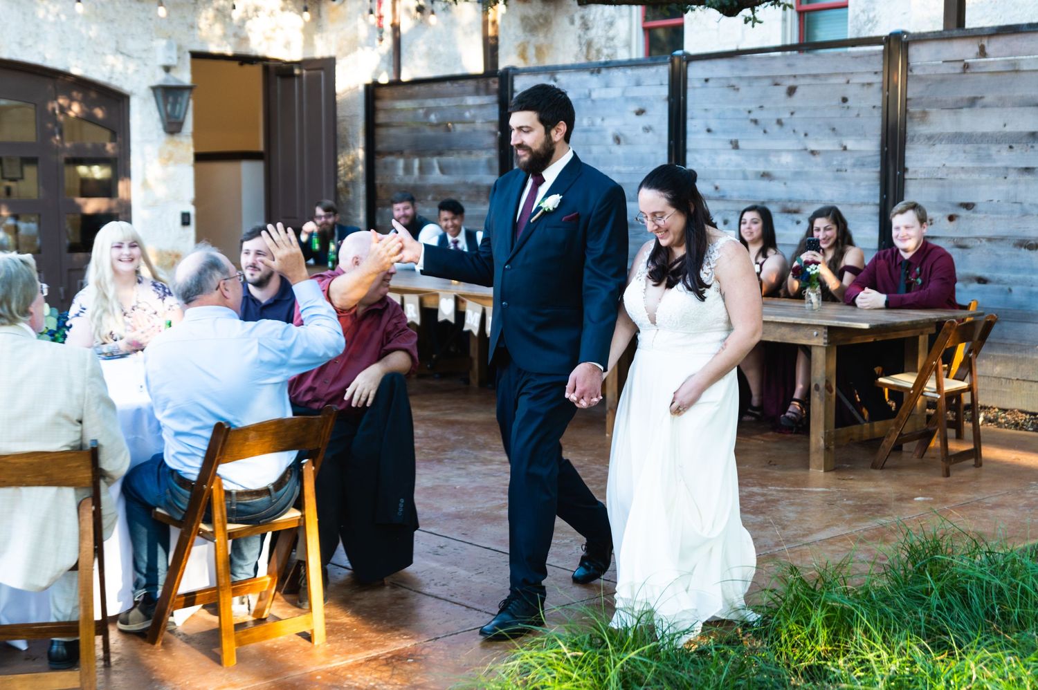 Newlyweds walk through reception venue with rustic decor and seated guests.