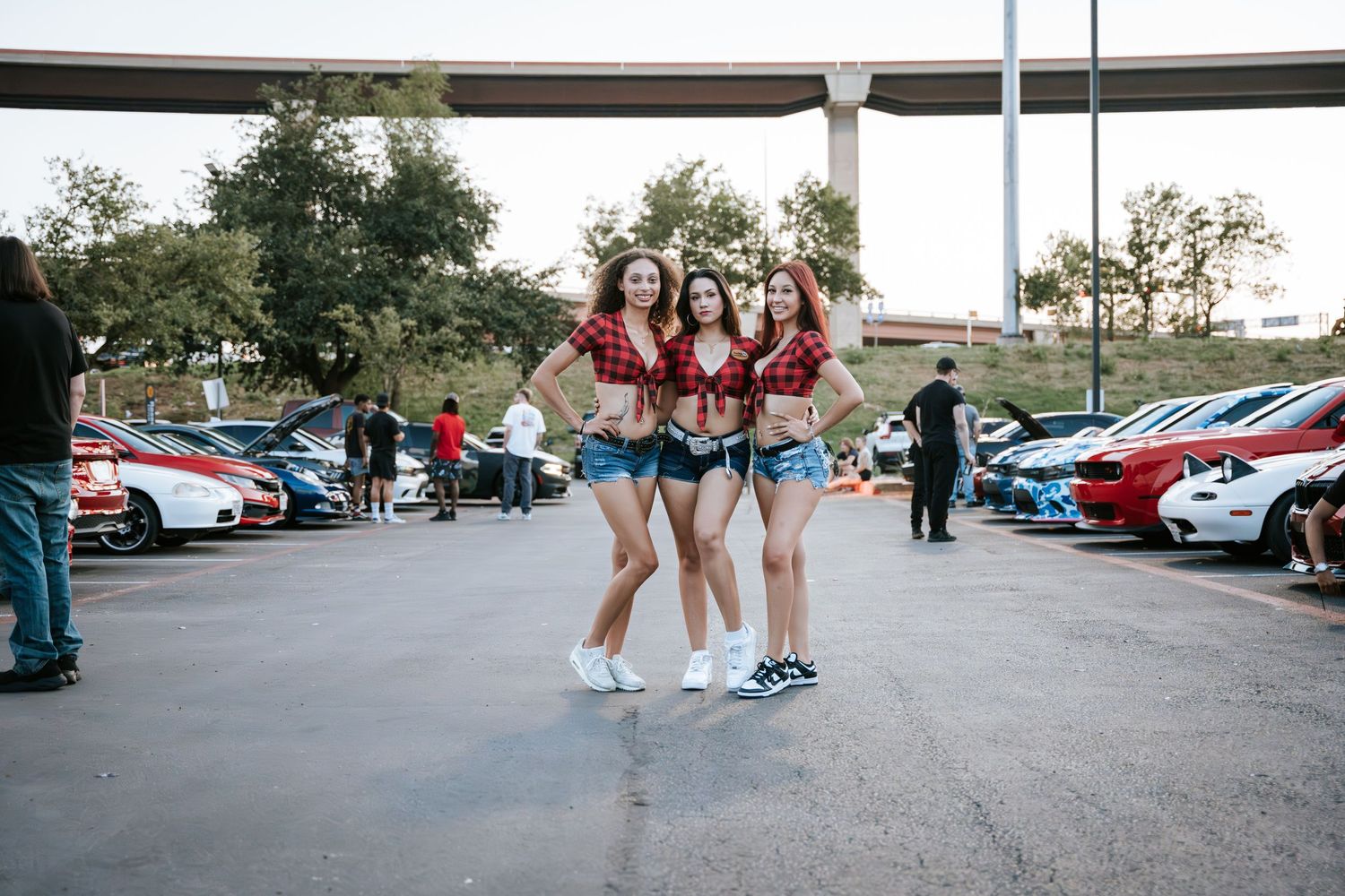 Small group in coordinated casual attire poses together at an outdoor car meetup event.