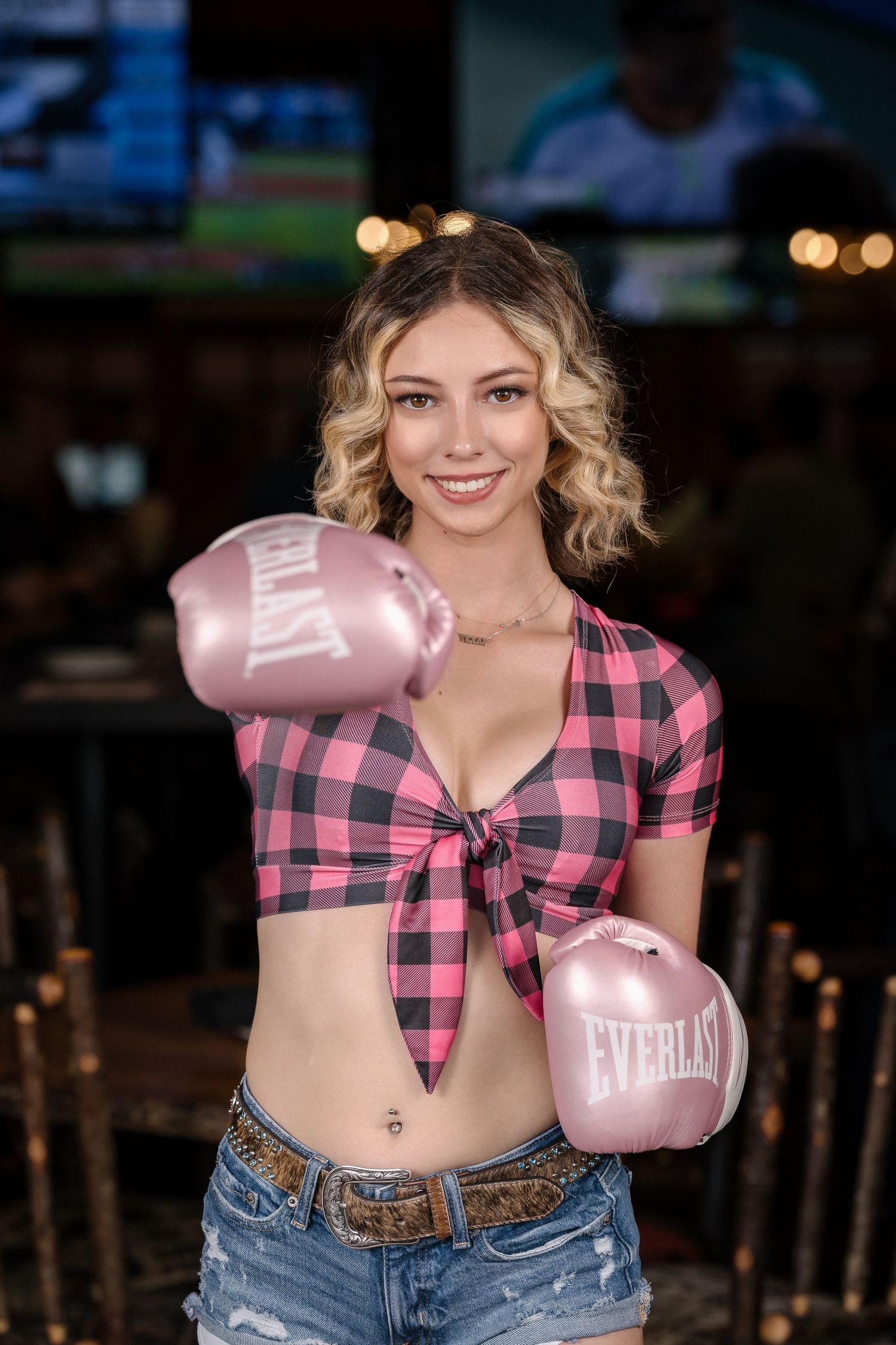 Model poses with pink boxing gloves wearing plaid crop top and distressed denim shorts.