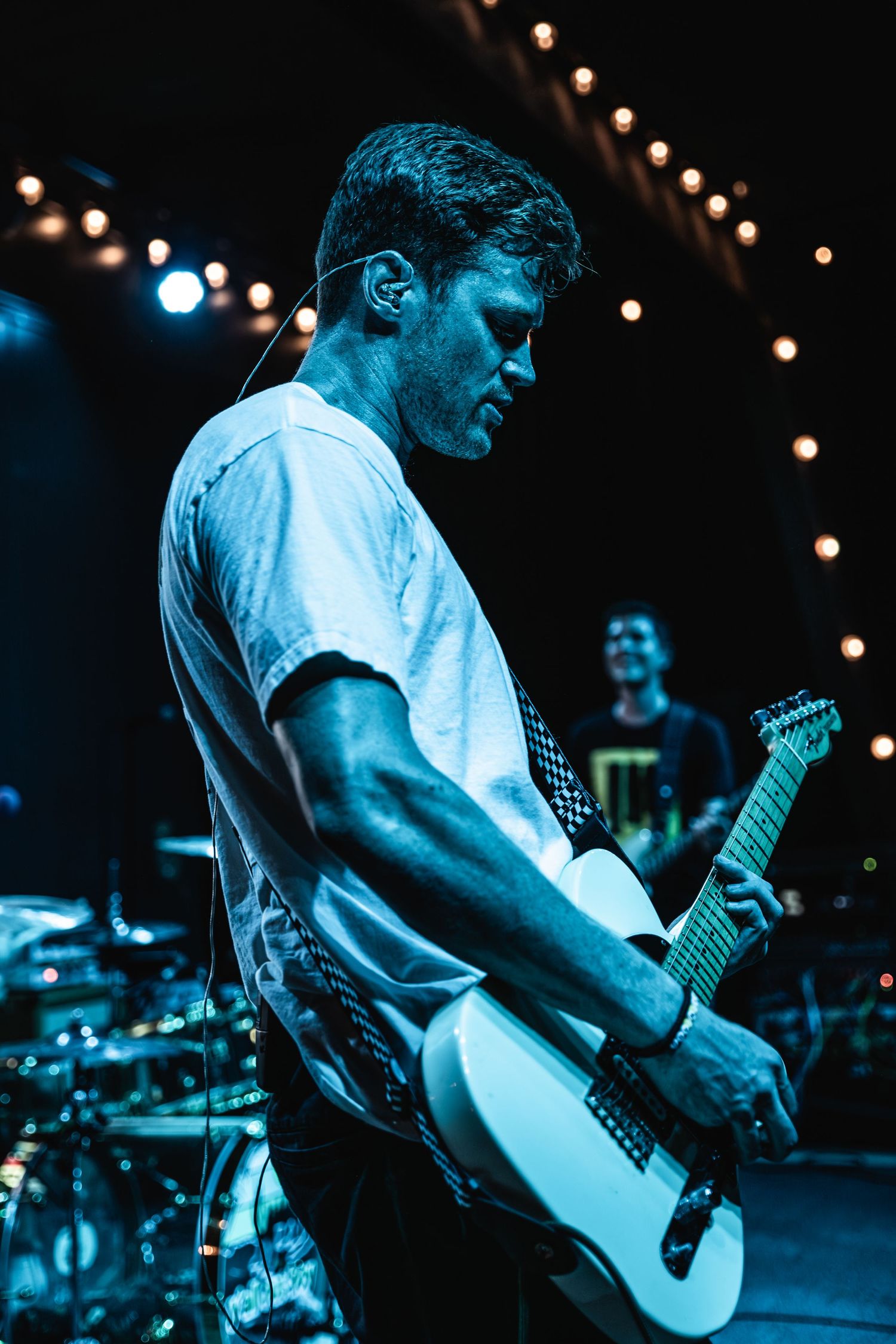 Guitarist in white t-shirt performing under moody blue stage lighting.
