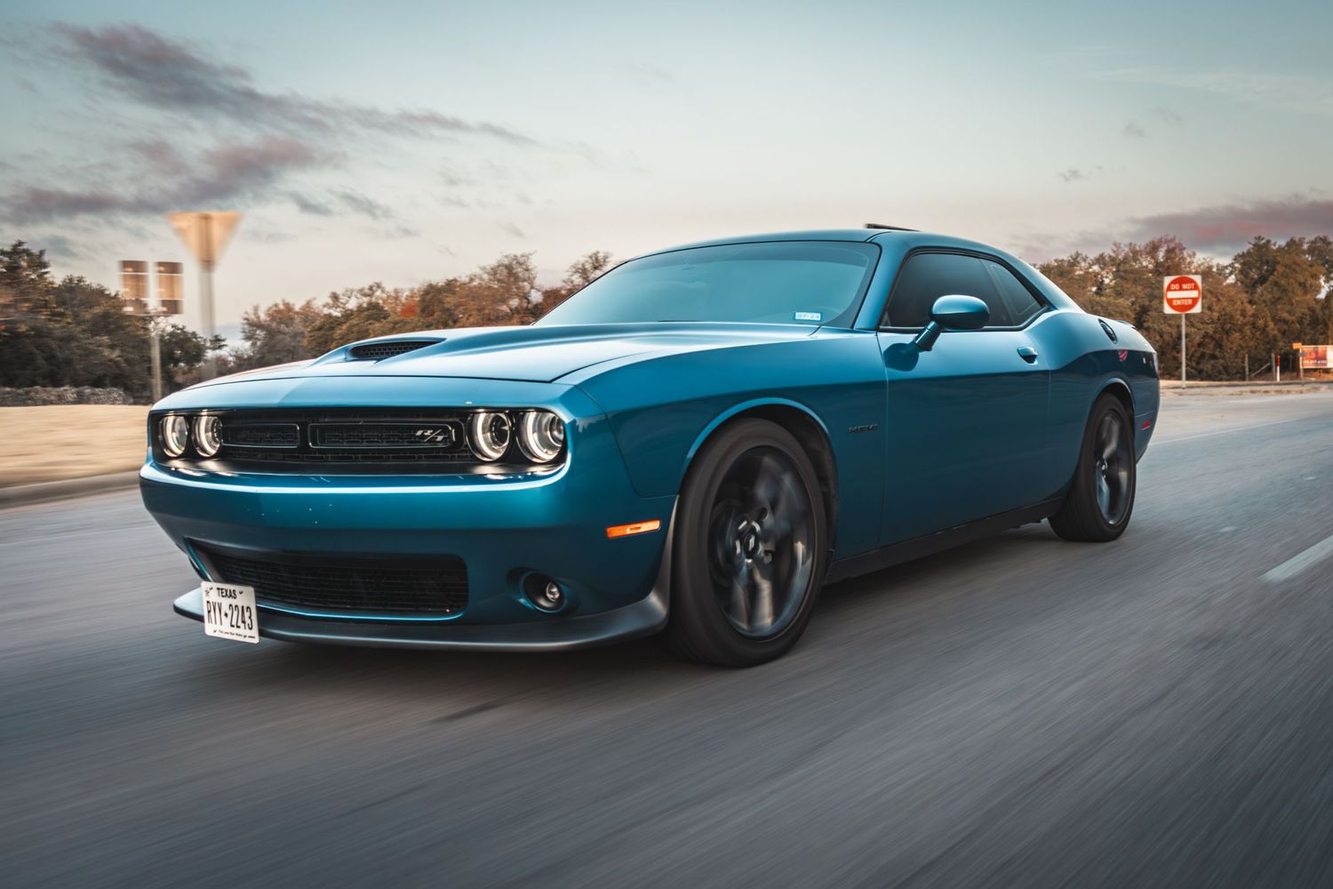 Metallic blue Dodge Challenger in motion on street at dusk.