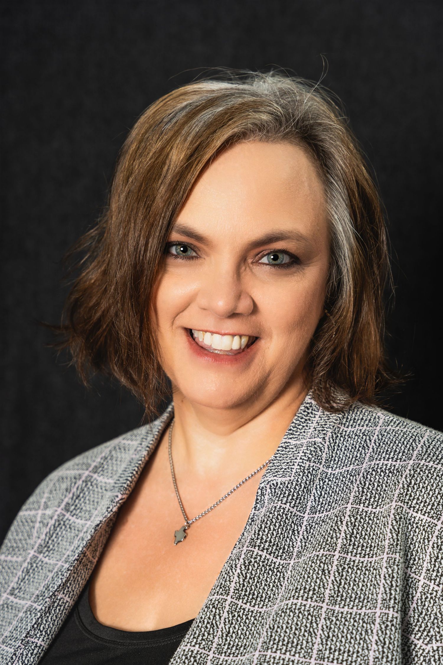 Business portrait showing warm smile and professional attire with textured grey blazer.